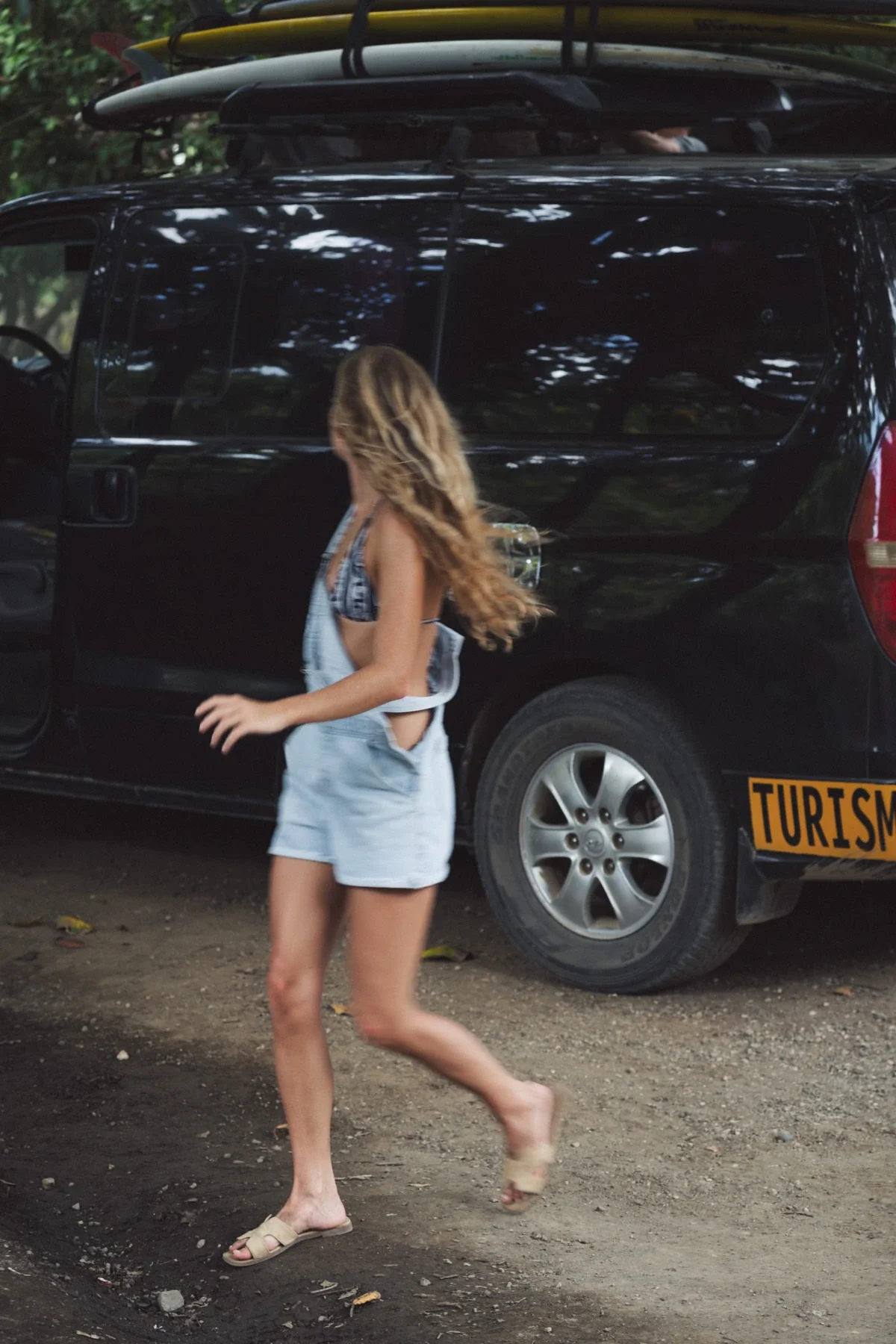Woman walking past a surf trip van loaded with a surfboard in Costa Rica, tourism vehicle ready for a guided surf adventure.