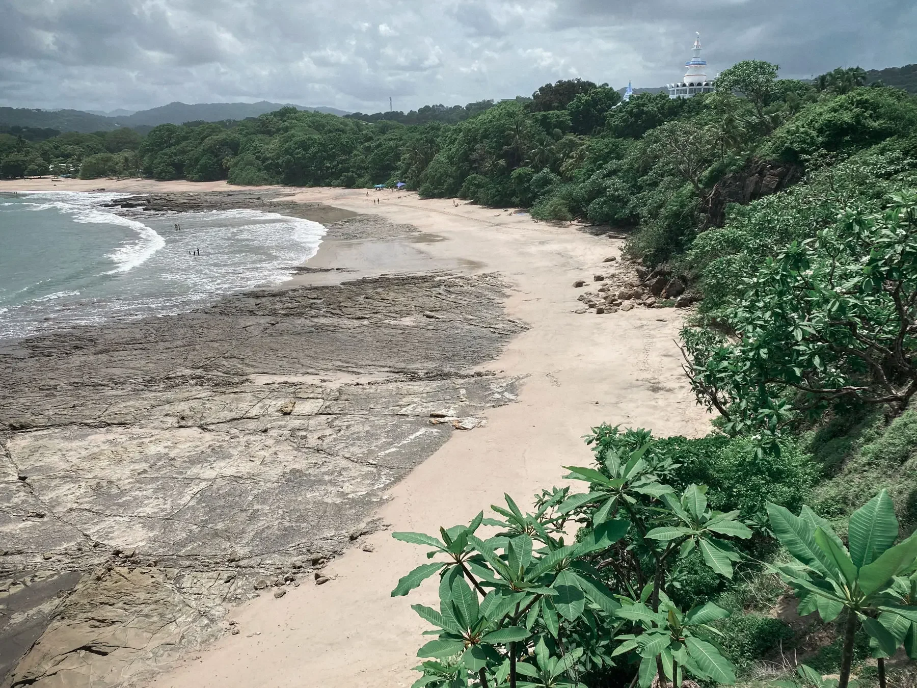 View of Playa Pelada Costa Rica from the hillside, sandy beach with natural tide pools, blue ocean and lush green trees