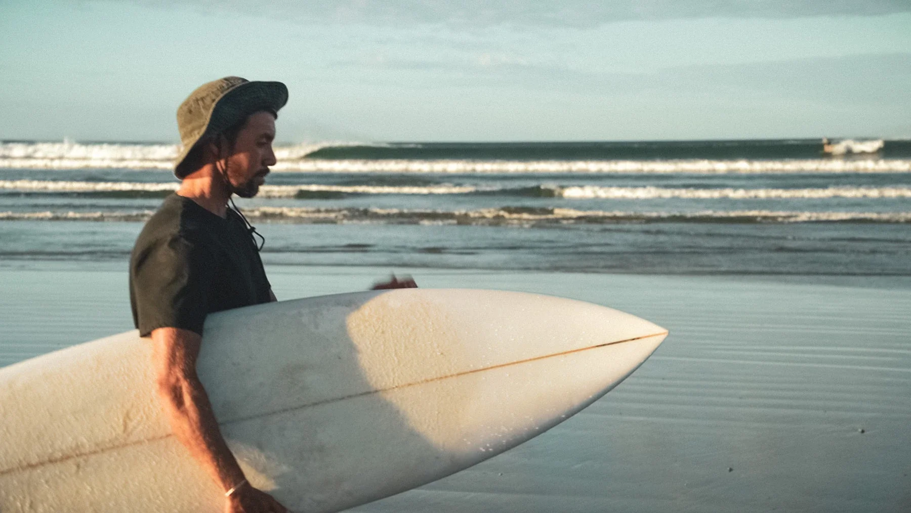 Surf instructor holding a surfboard on the beach at Playa Guiones Nosara Costa Rica, ocean waves in the background.