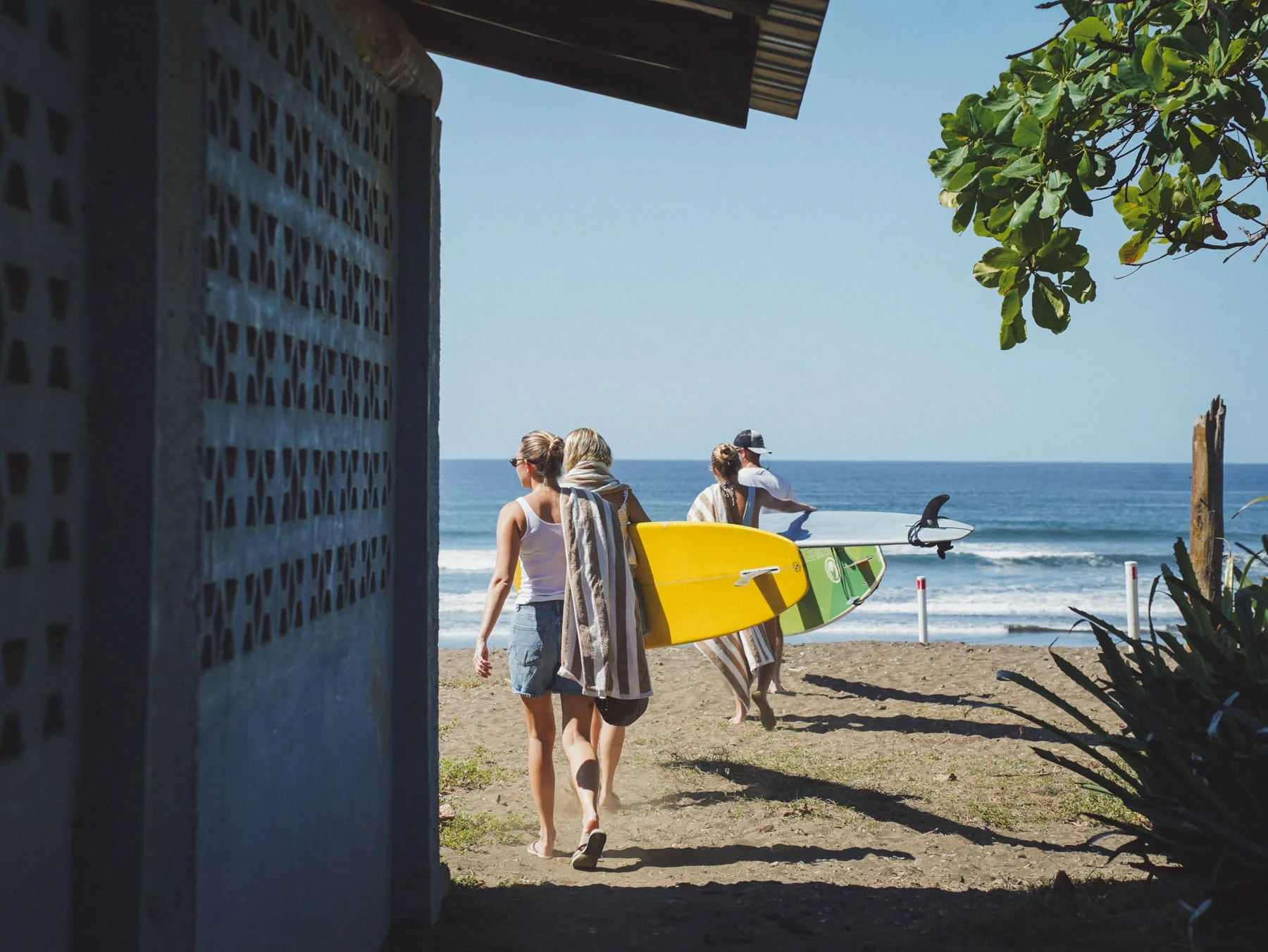 Family heading to the beach with surfboards during a surf trip in Costa Rica, tropical plants and colorful walls in the background.
