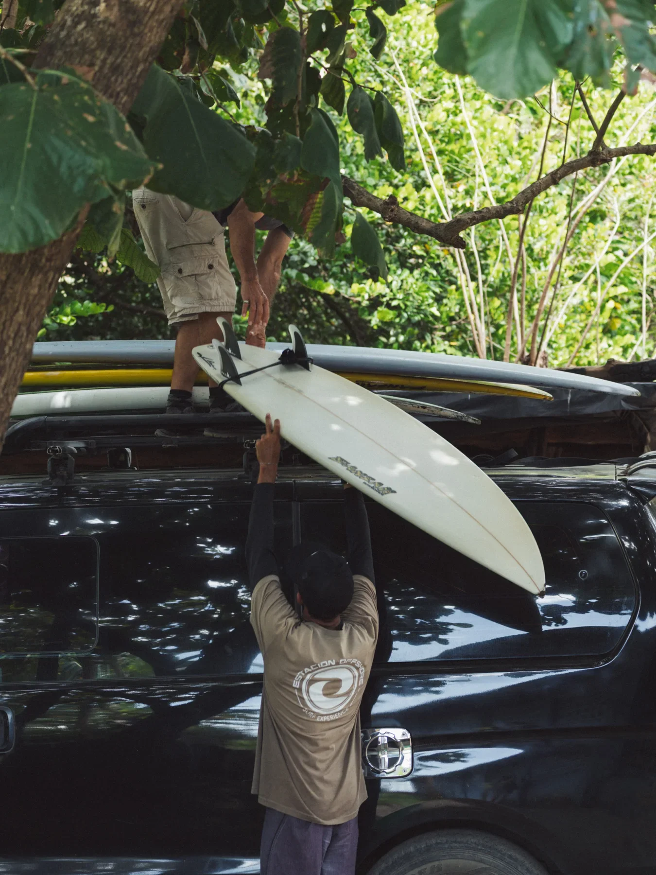 Two surfers are loading surfboards onto the roof of a van during surf trip in Costa Rica