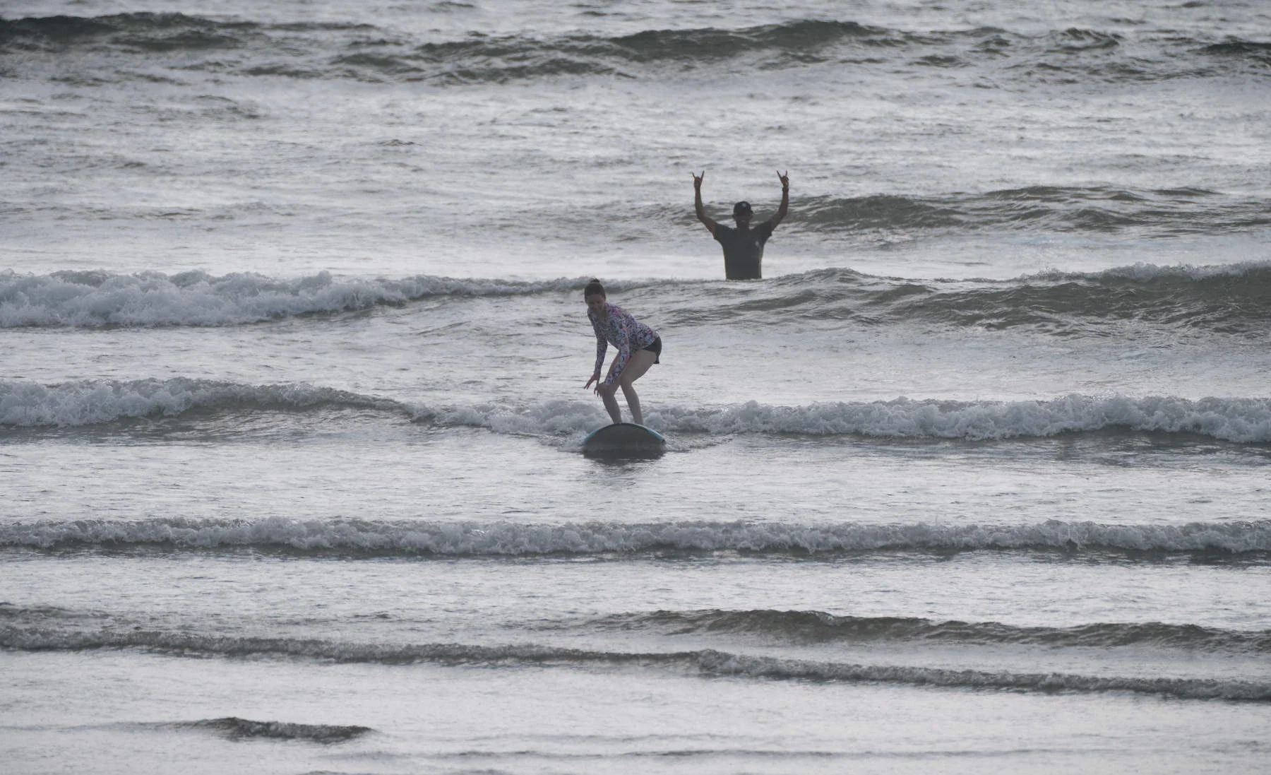 Young girl riding wave during surf lesson at Playa Guiones Nosara, surf coach in the water giving encouragement