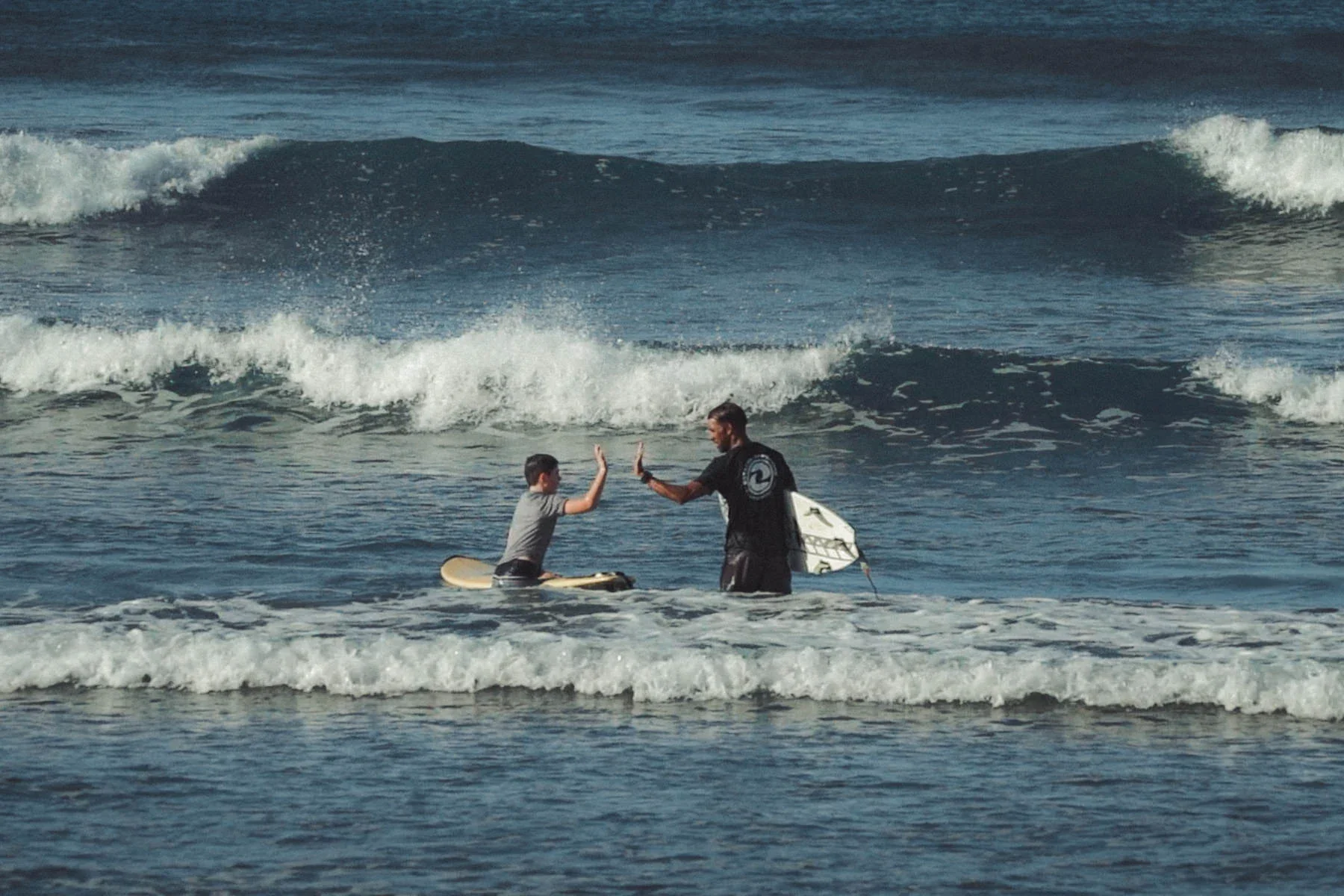 Surf instructor and young student celebrating after a surf lesson at Playa Guiones Costa Rica, surfboards nearby and waves in the background.