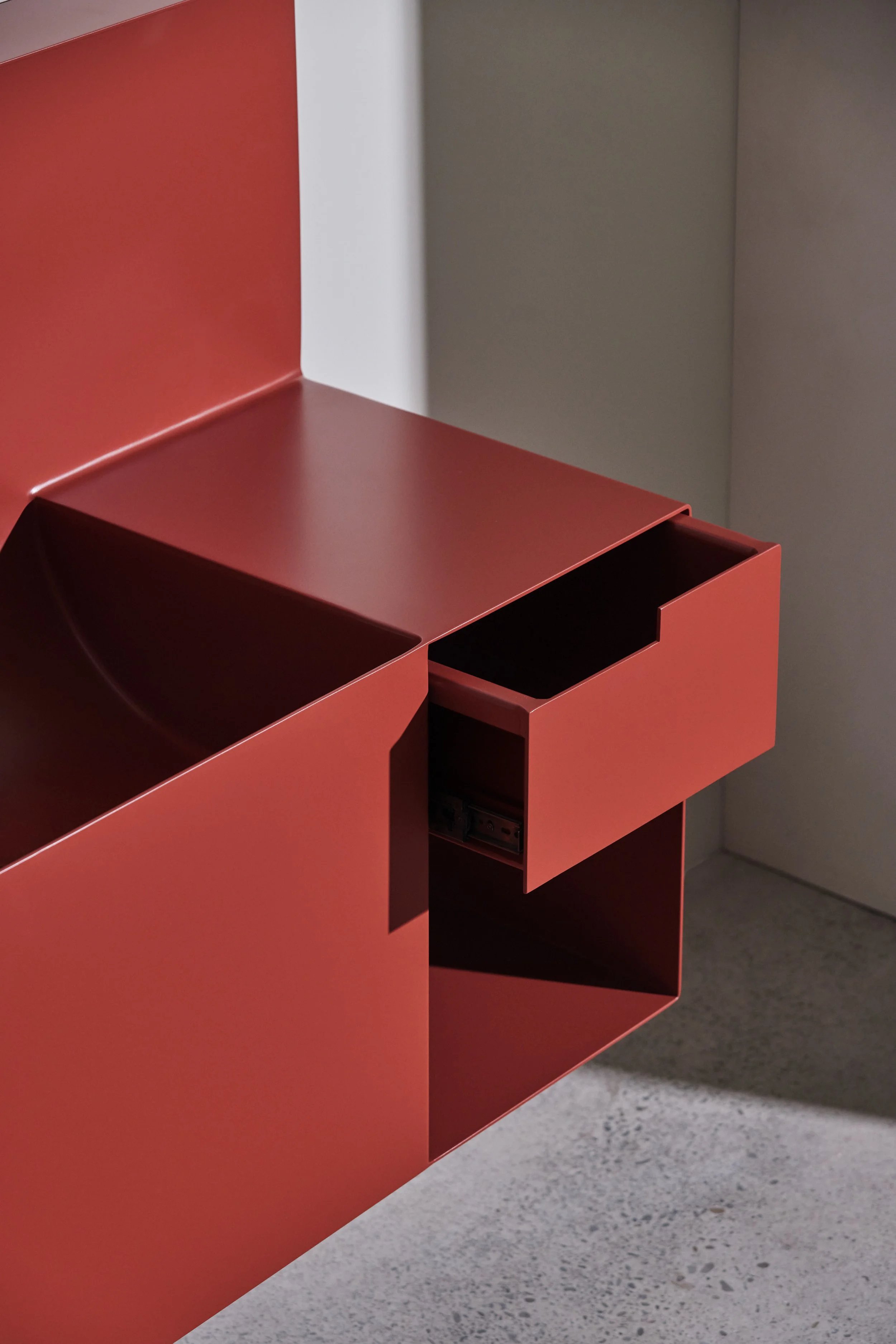 Close-up of a modern, red wall-mounted cabinet with open compartments, set against a gray wall and floor.