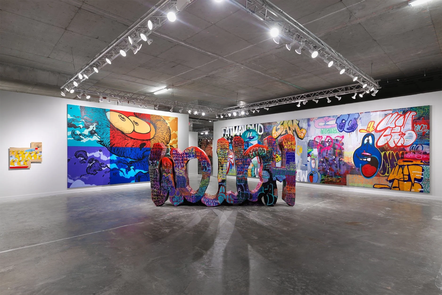 Art gallery interior with colorful graffiti-style paintings on walls and a central abstract sculpture.
