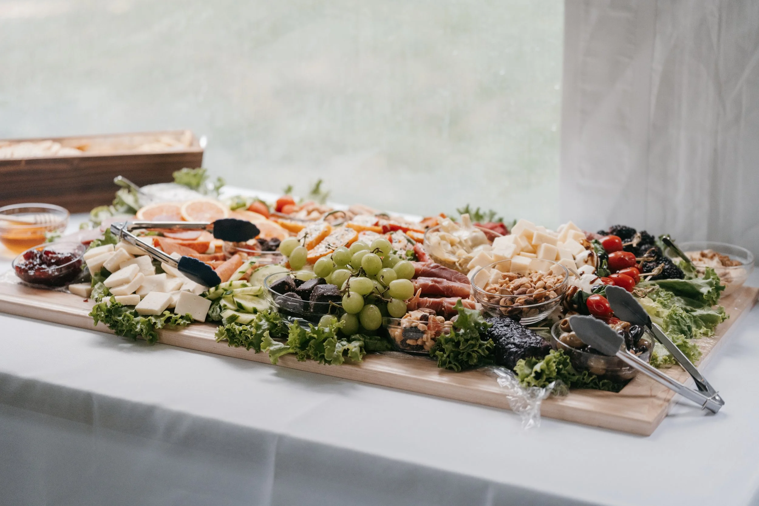 Luxury grazing table with artisan cheeses, cured meats, fresh fruit, nuts, and vegetables styled for an elegant wedding or private event.
