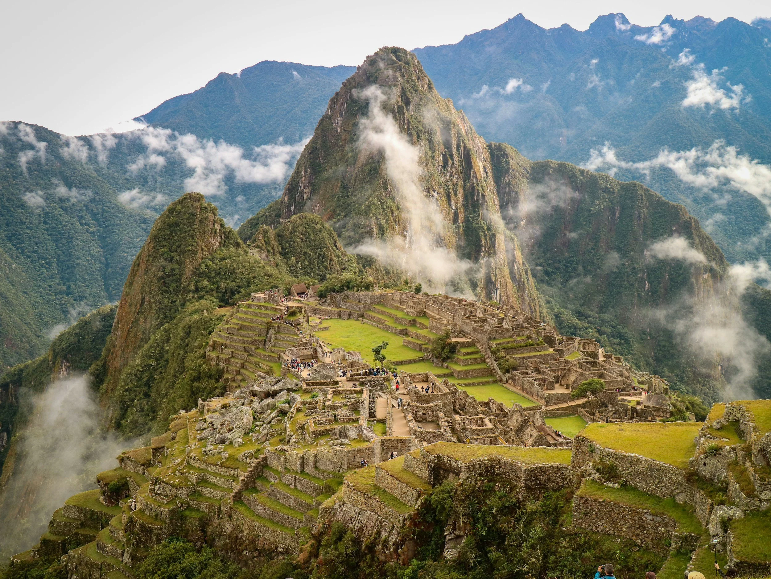 Ancient Incan ruins at Machu Picchu on a mountain with green terraces, surrounded by misty mountains and clouds.