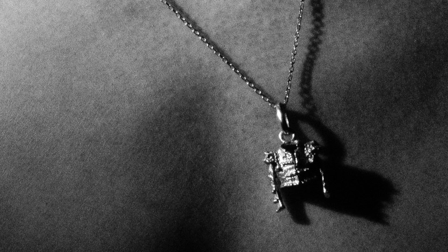 Collier en chaîne avec pendentif représentant une ferme ou un bâtiment, en métal argenté ou orné de détails.