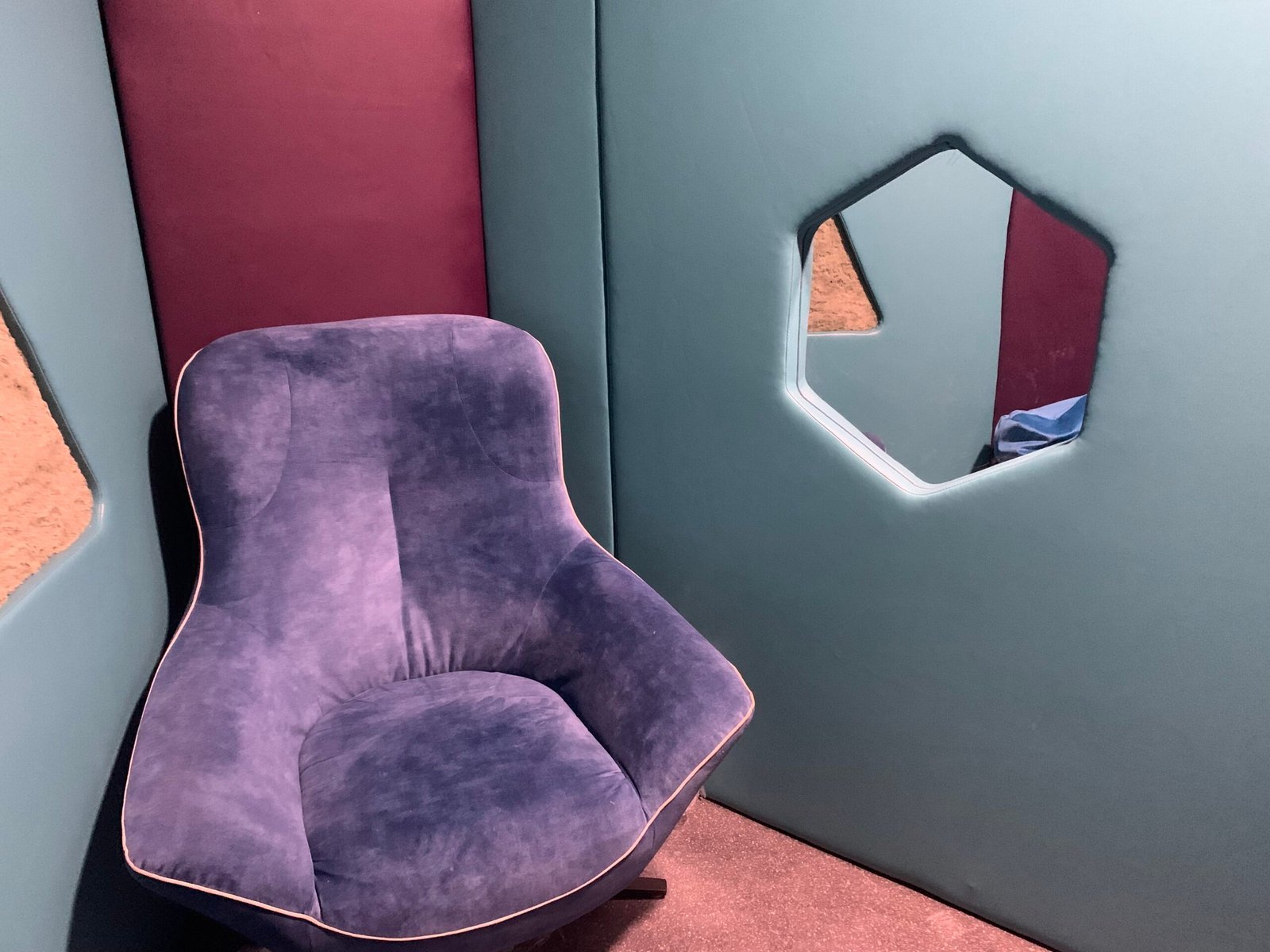 A plush purple velvet armchair inside a padded blue and burgundy sensory booth with a hexagonal window cut-out.