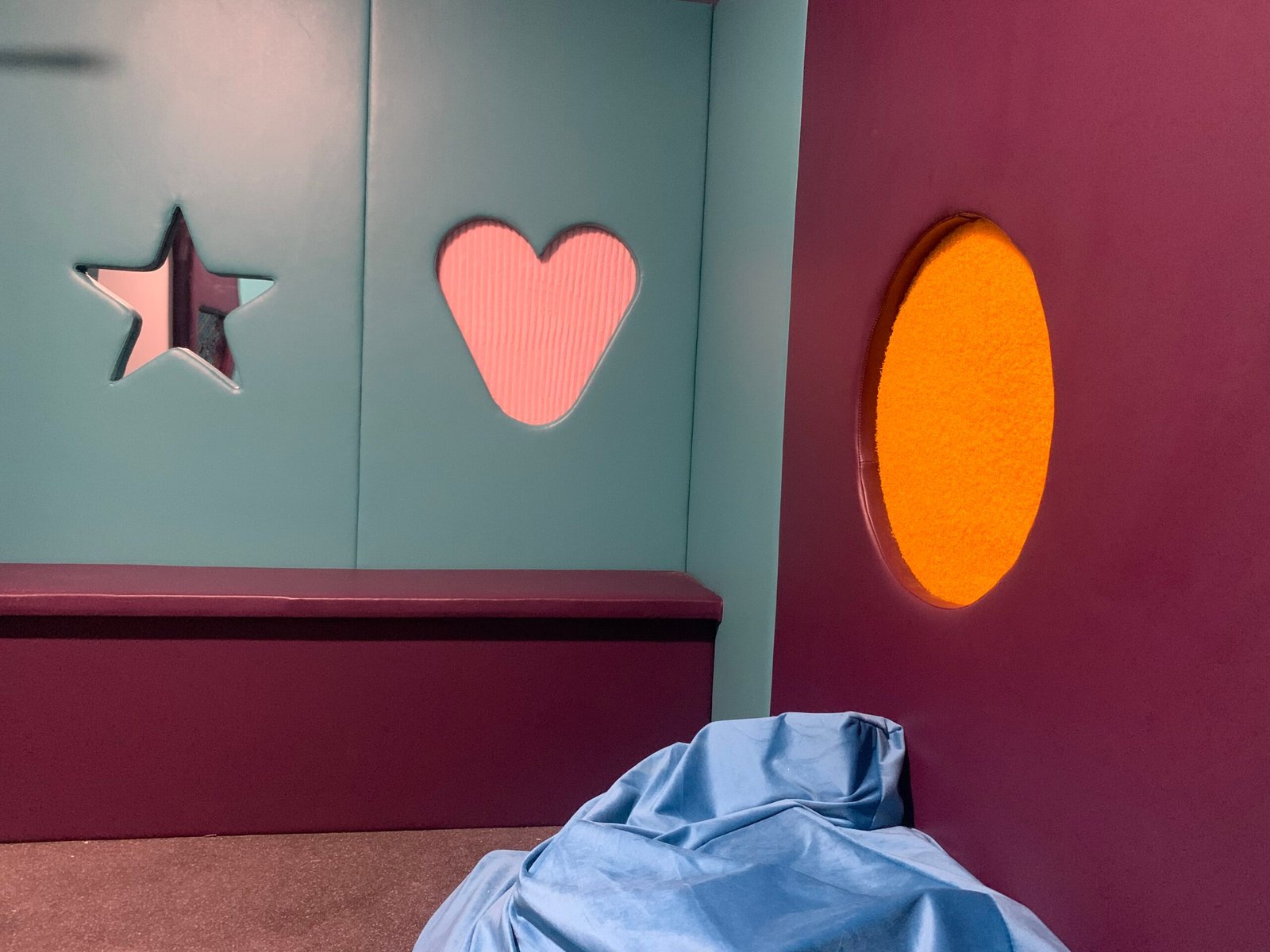 Interior of the sensory hub showing padded walls with star, heart, and circular sensory features alongside a soft blue beanbag.