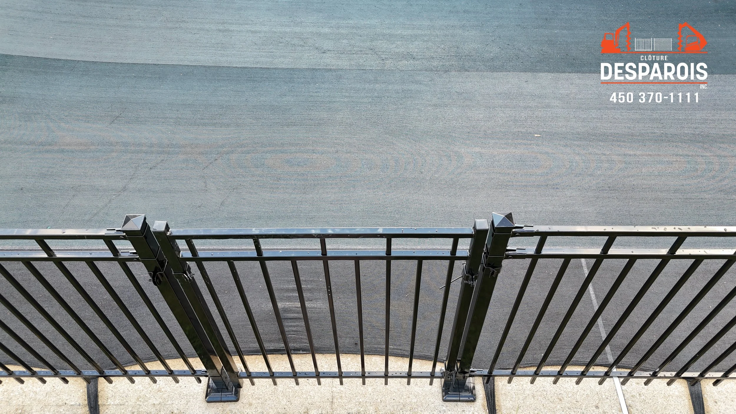 vue de dessus d'une clôture noire en métal séparant un trottoir d'une cour ou d'un terrain de tennis vide.