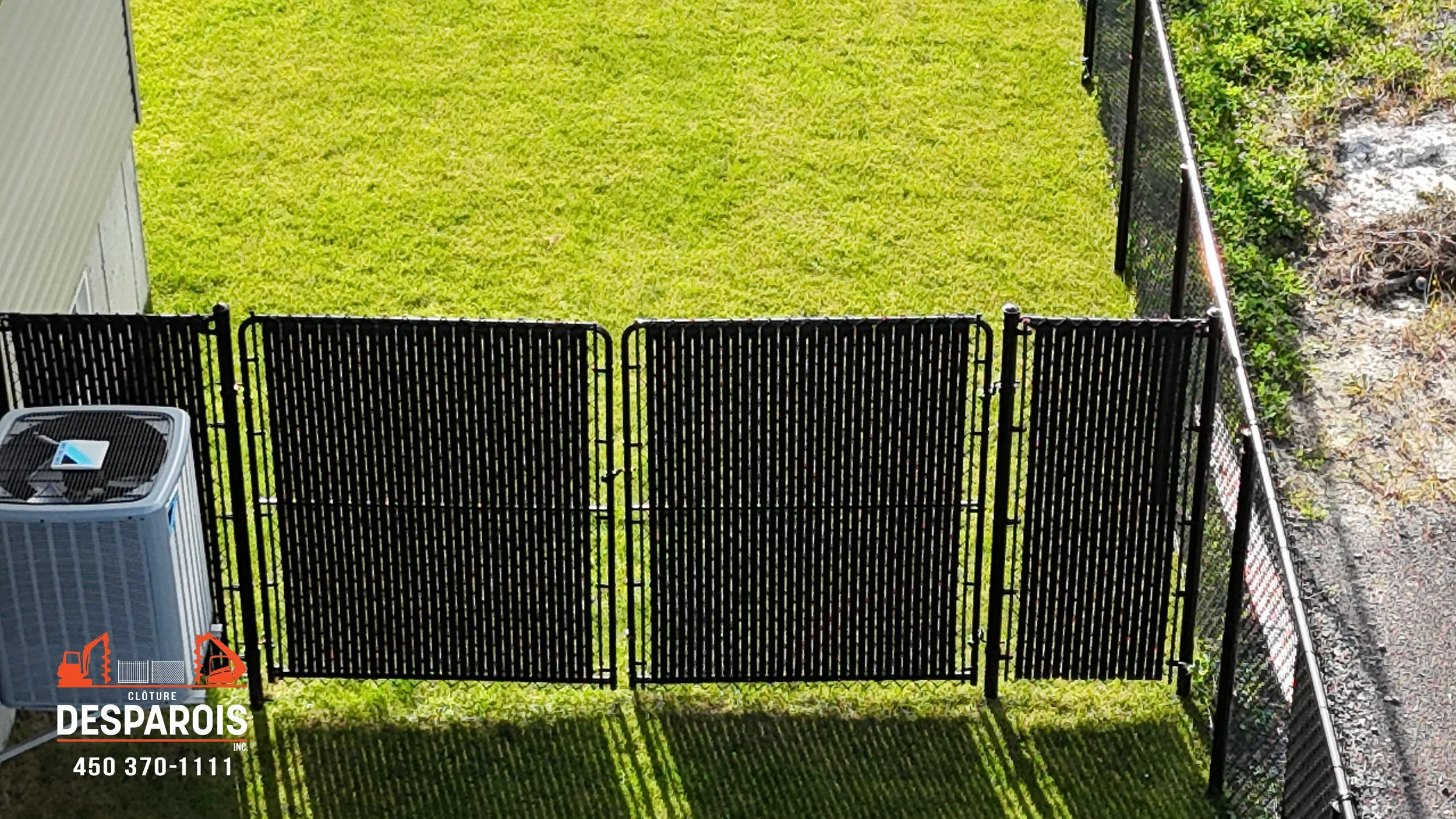 Une clôture en métal noir séparant un espace vert, avec une unité de climatisation à gauche et une chaîne de fence droite.