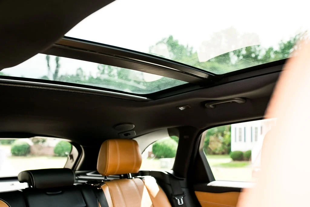 The interior of a car showing a sunroof, leather seats, and a view of a residential neighborhood through the windows.