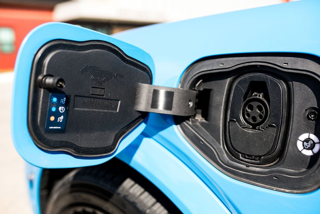 Electric vehicle charging port with open cover on blue car