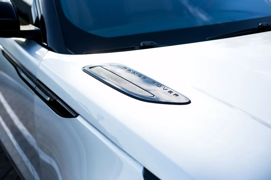 Close-up of the hood of a white Range Rover truck, showing the Range Rover badge on a metallic vent.