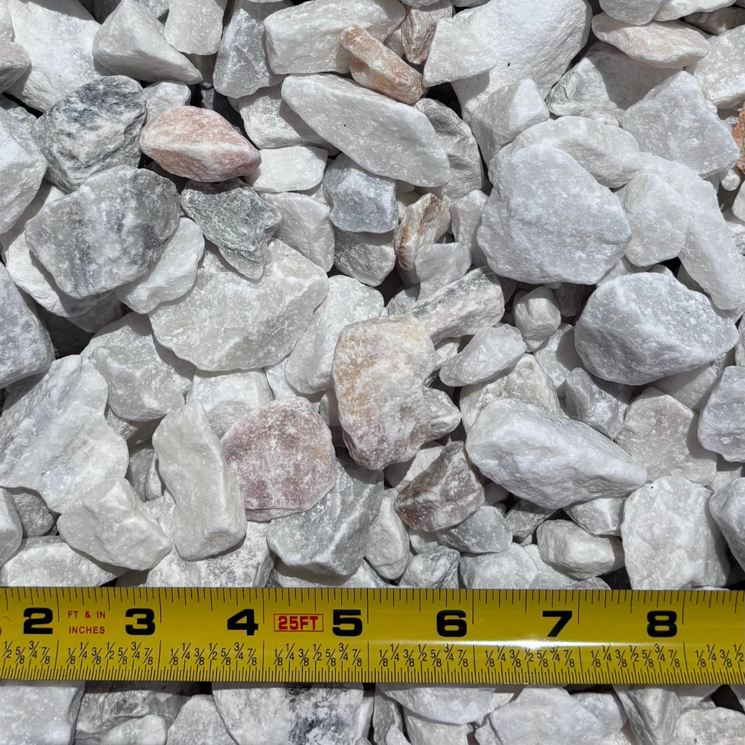 Close-up of white and light-colored gravel stones with a yellow measuring tape showing inches at the bottom.