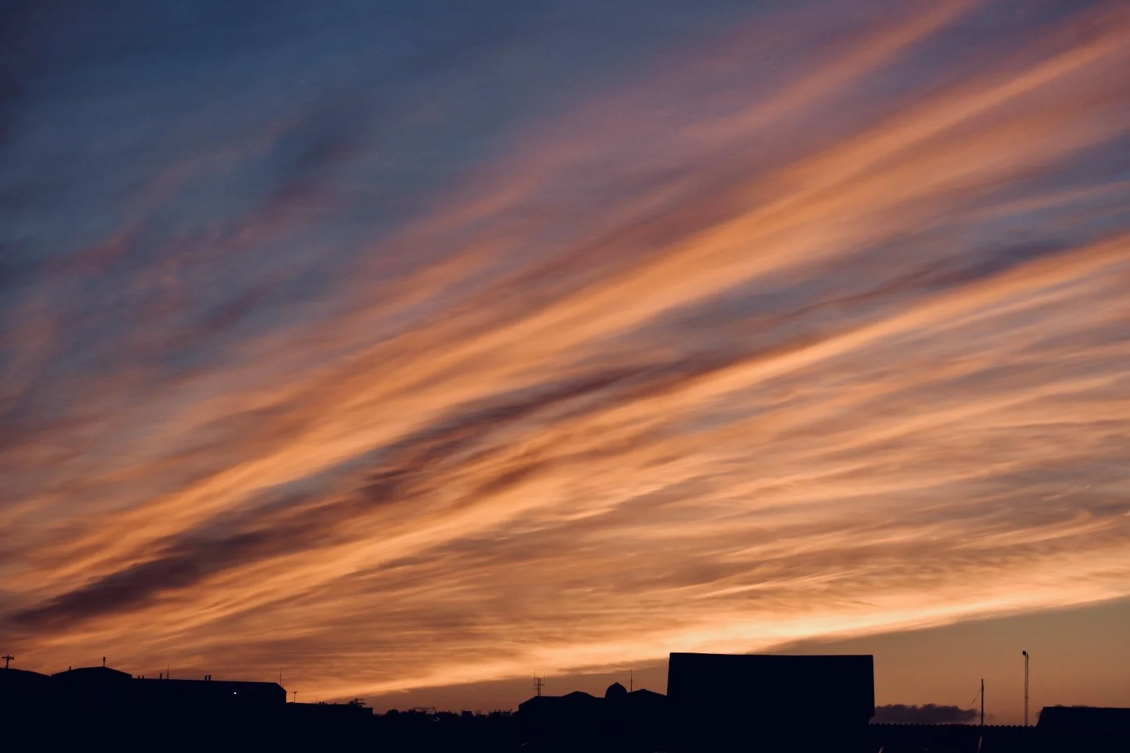 Sunset sky with orange and pink clouds over silhouetted buildings.