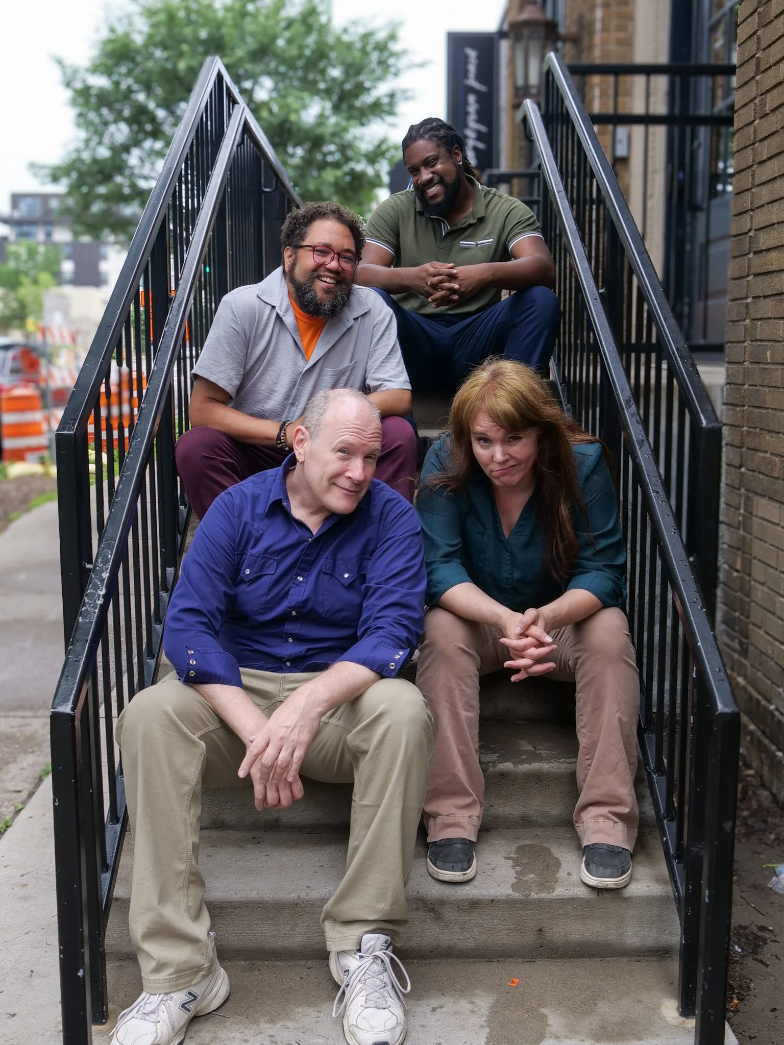 Four people sitting on a set of concrete steps making various facial expressions.