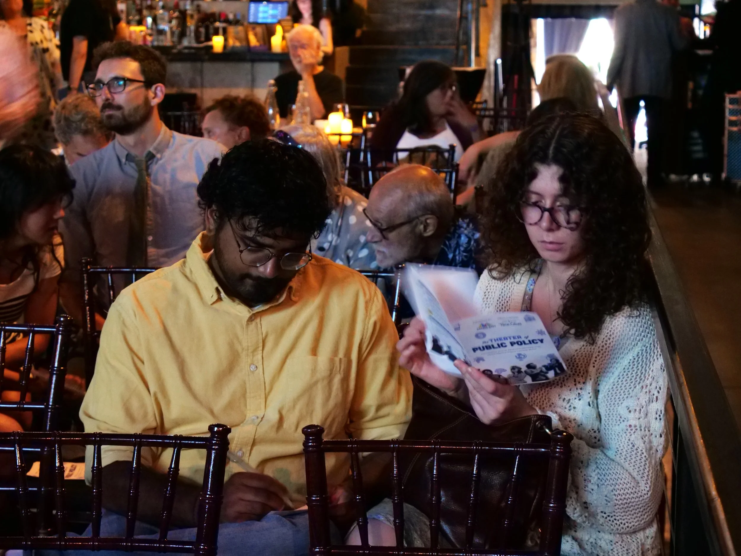  Two audience members check out the program and write questions for the guests to be answered live onstage. 