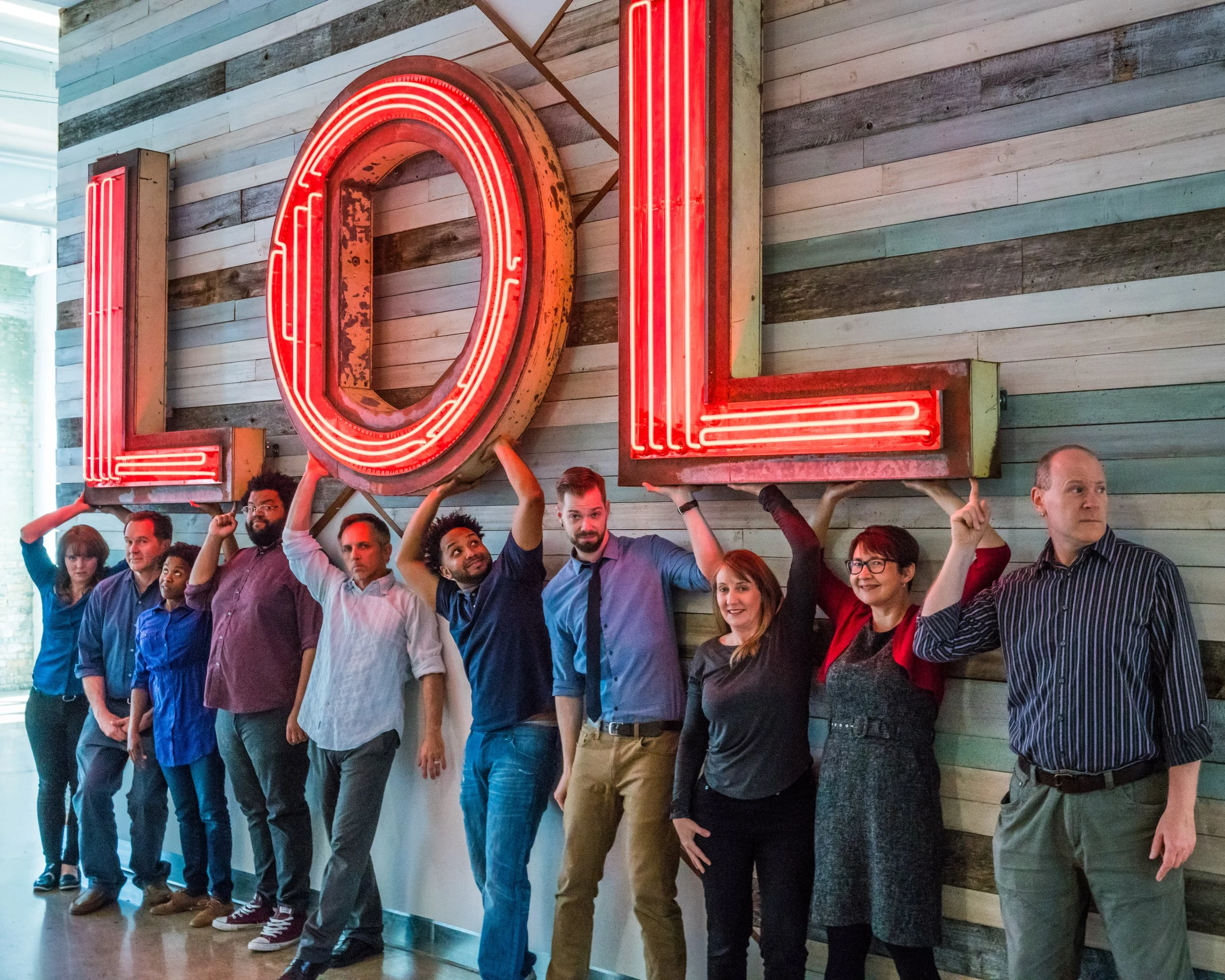 A photo of cast members of Danger Boat Productions standing in front of a neon LOL sign.