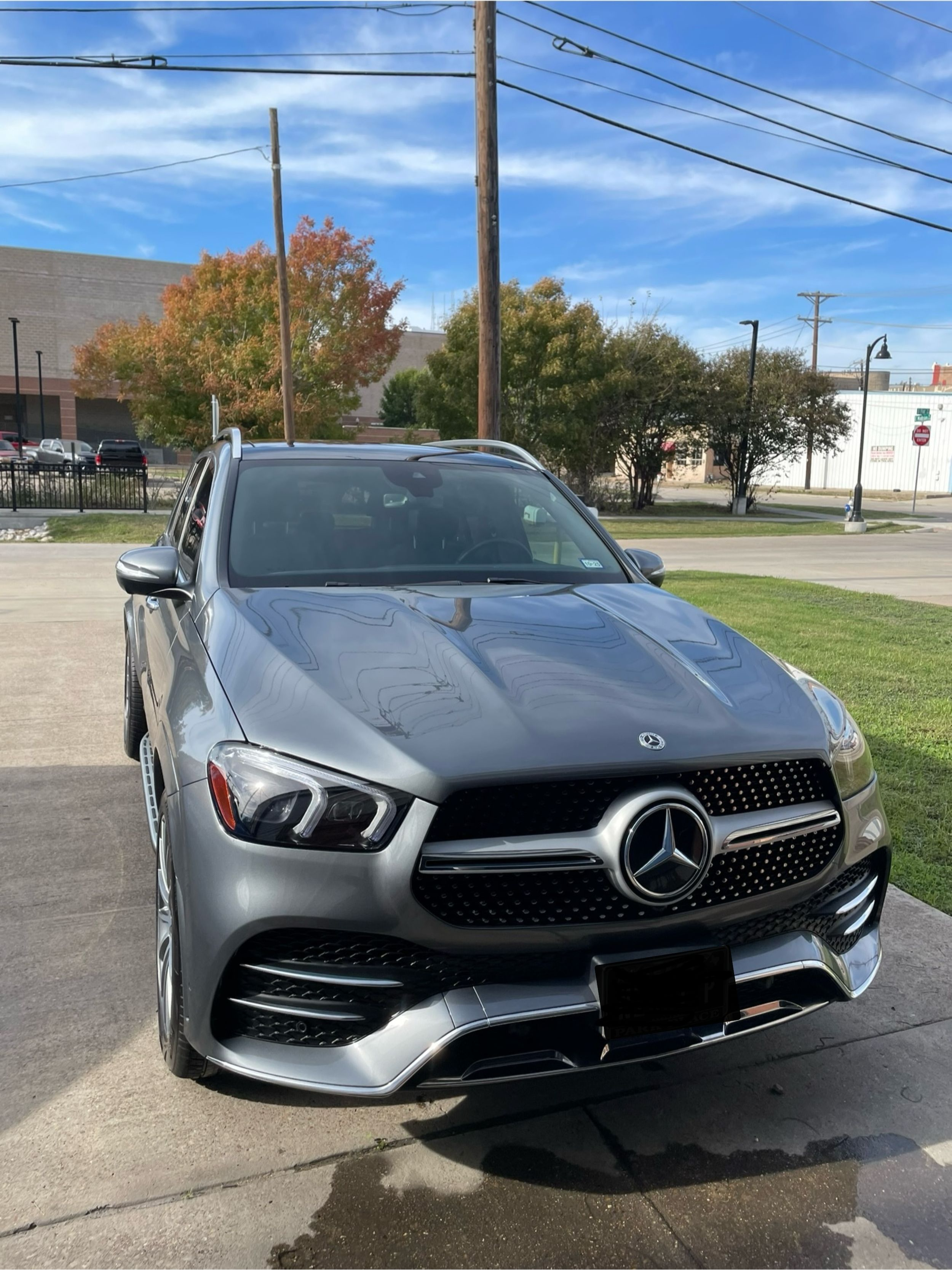 Silver Mercedes-Benz parked on a concrete surface with autumn trees and power lines in the background.