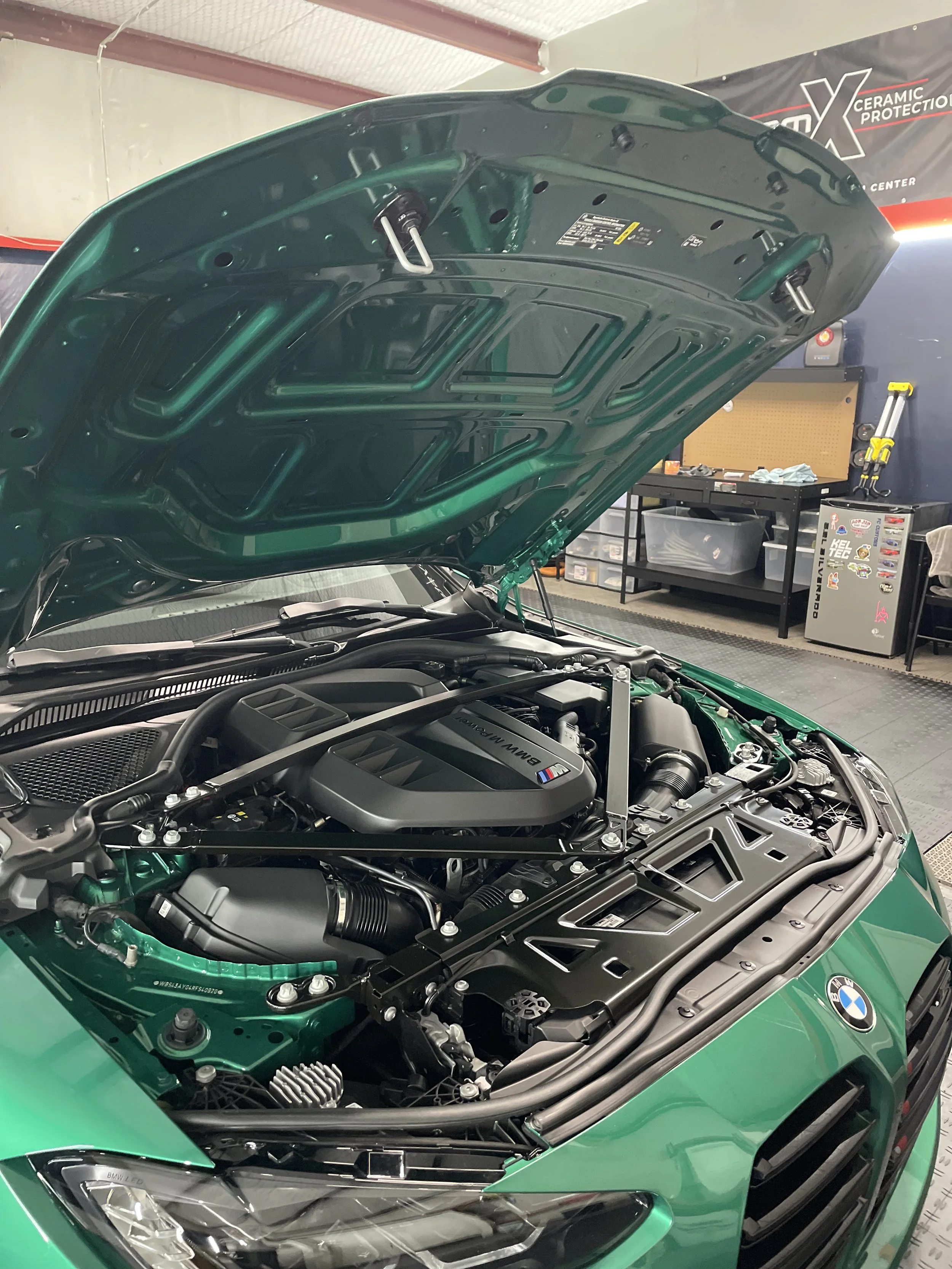 Open hood of a green BMW M4 engine bay in a workshop.