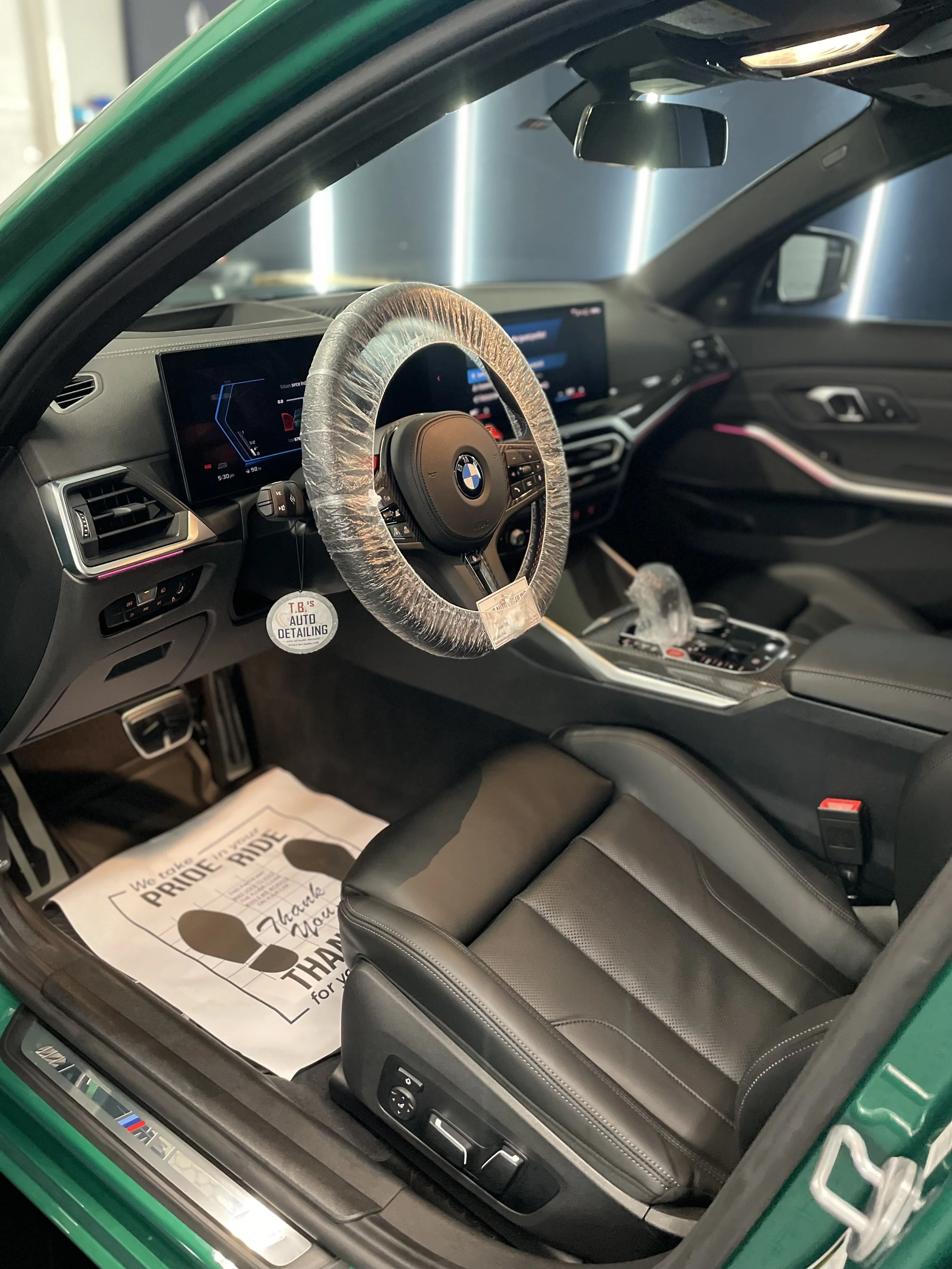 Interior of a BMW M4 vehicle with a wheel cover, digital dashboard, and leather driver seat, showroom background.