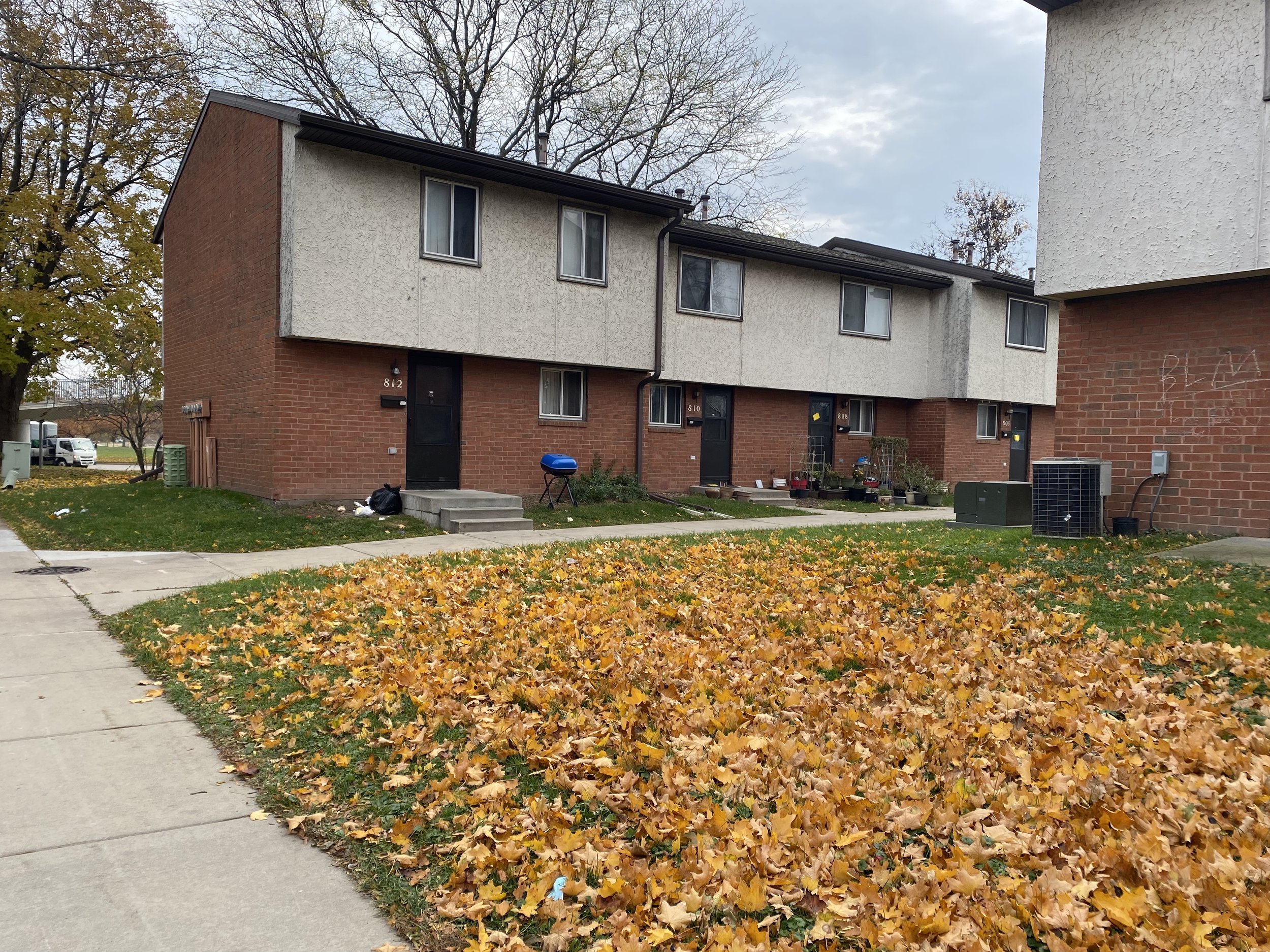Two-story brick and stucco townhomes. Fallen leaves cover a lawn in front of the building.