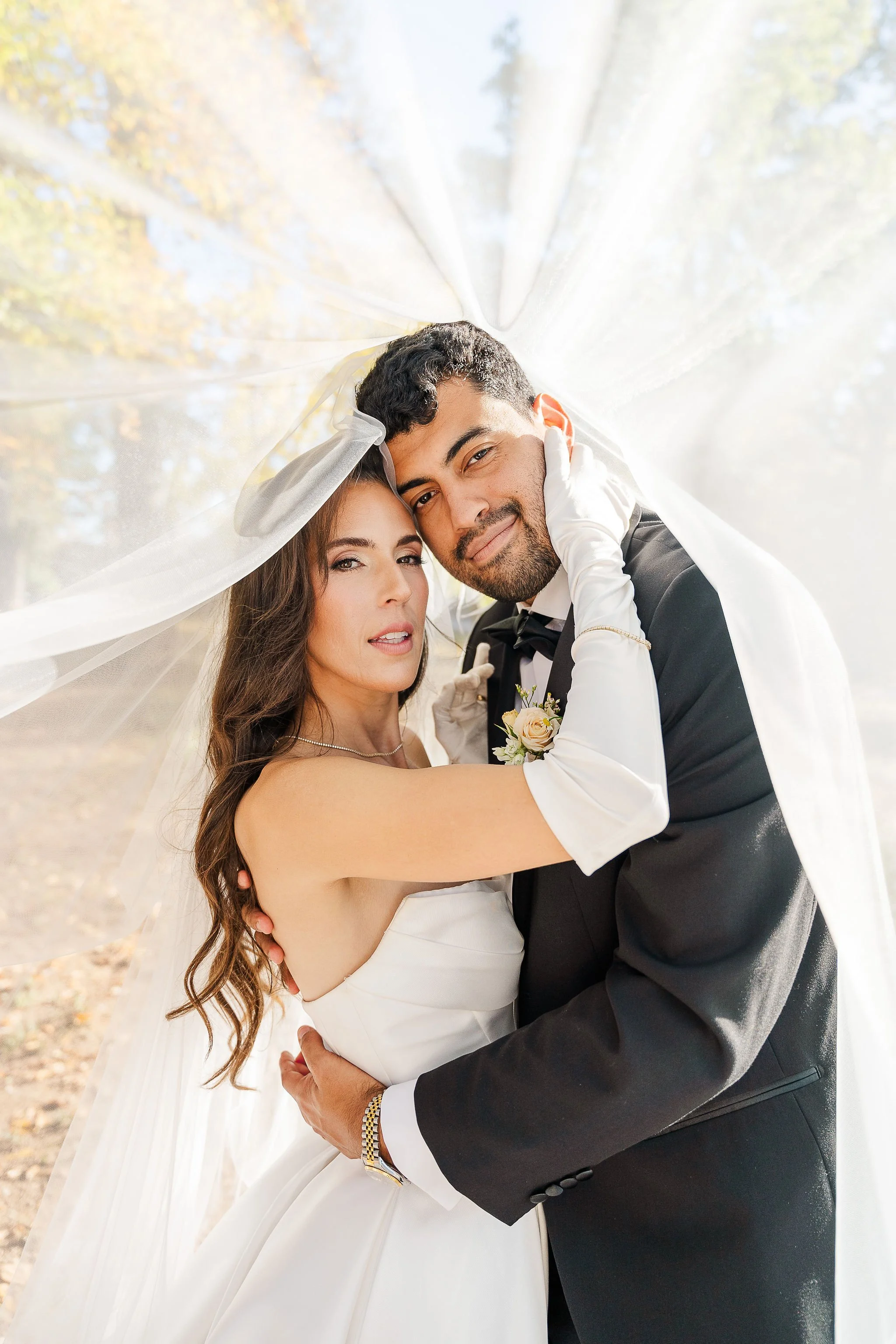 Bride and groom embracing under a long cathedral veil held overhead, demonstrating the under-the-veil portrait technique