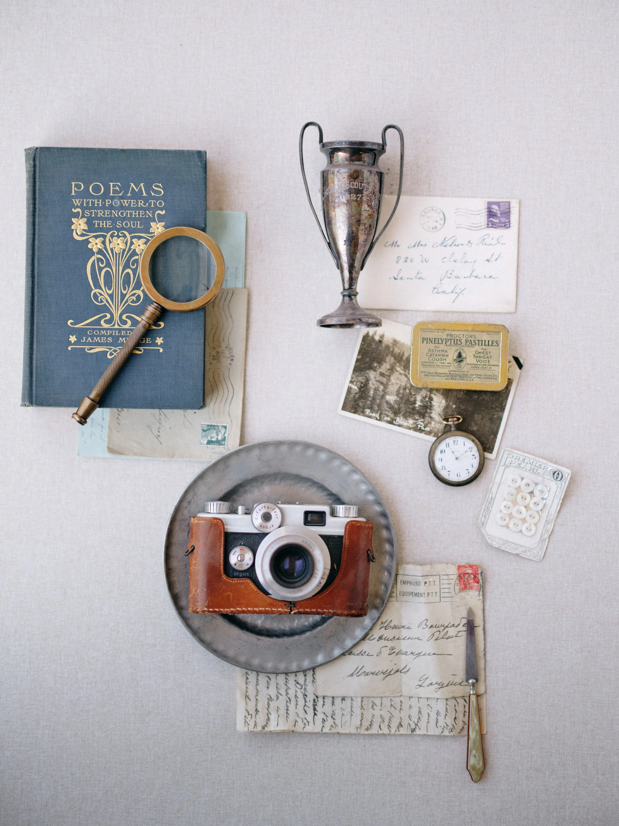 Vintage flat lay photography with antique camera, poetry book, postcards, and brass magnifying glass on light gray surface