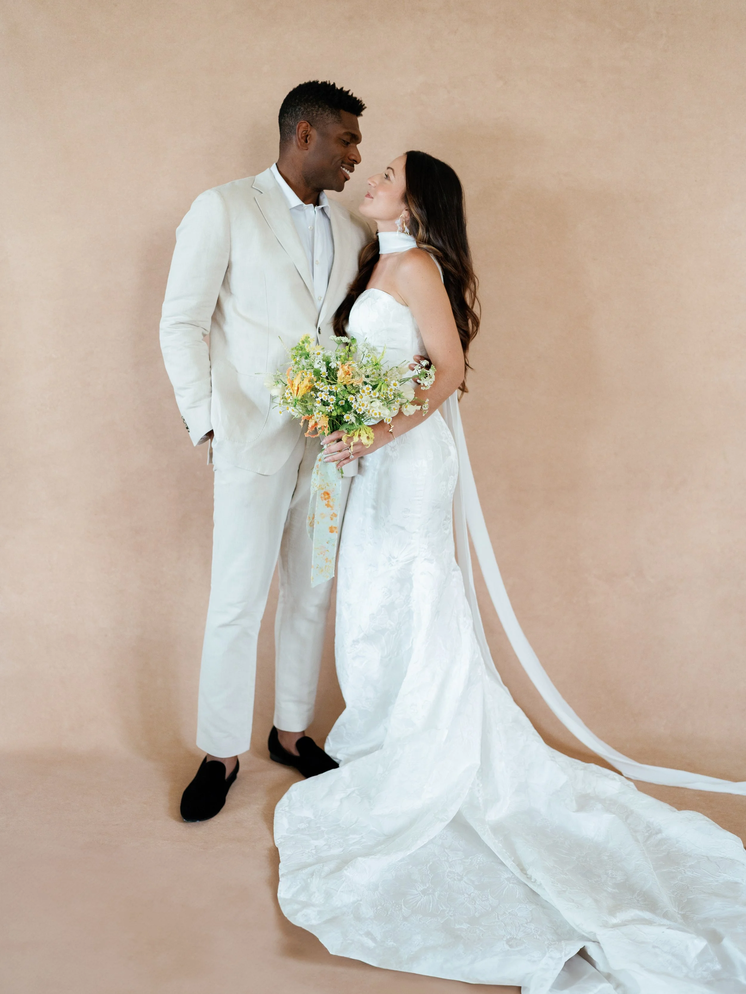 Full-length bridal couple portrait posed on an 8x14 photography backdrop with gown train visible