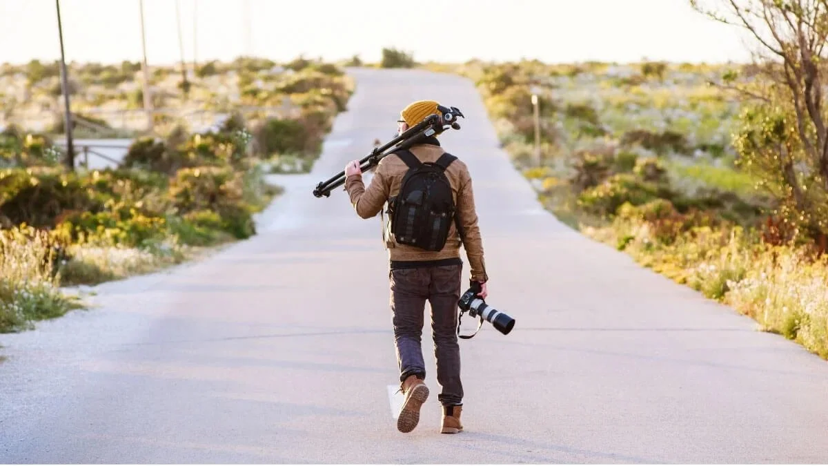 Photographer walking on open road carrying camera and tripod on location