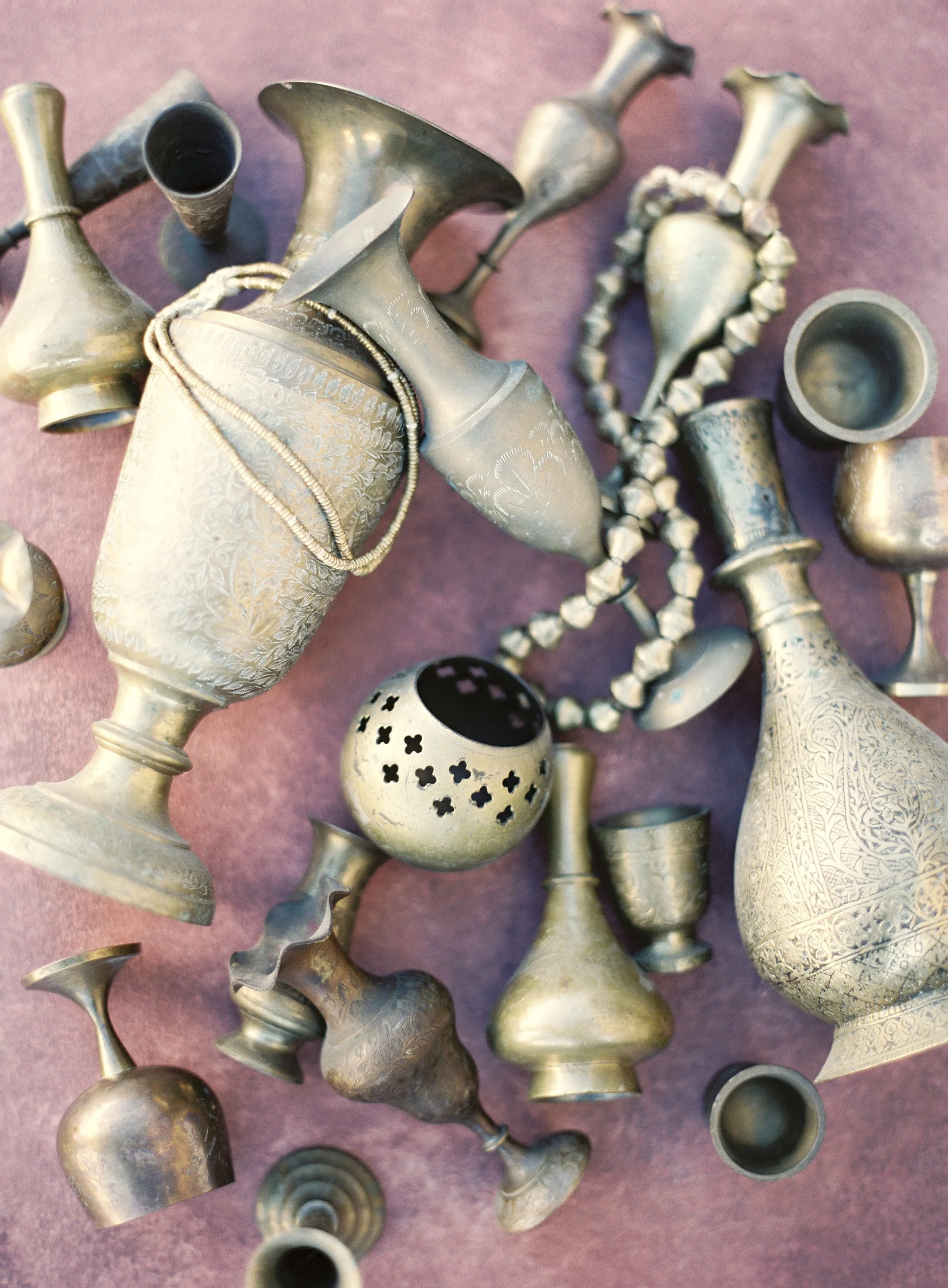 Flat lay photography of vintage brass vessels and beaded necklace arranged on purple pink styling surface