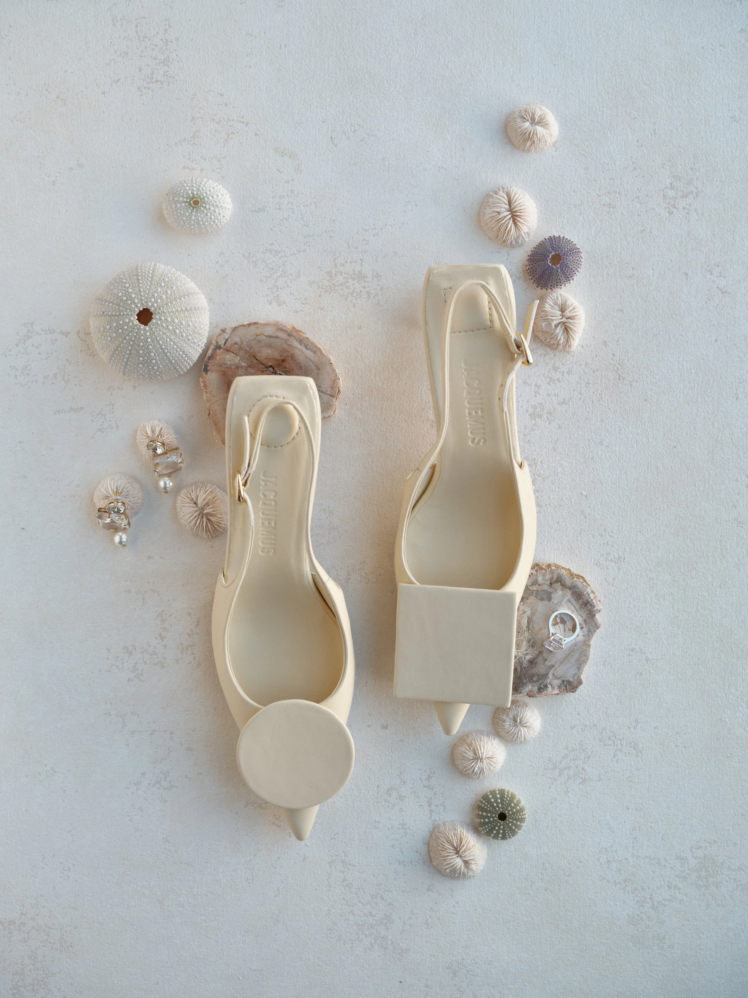 bridal shoes and wedding ring flat lay on textured canvas backdrop with shells and soft natural light