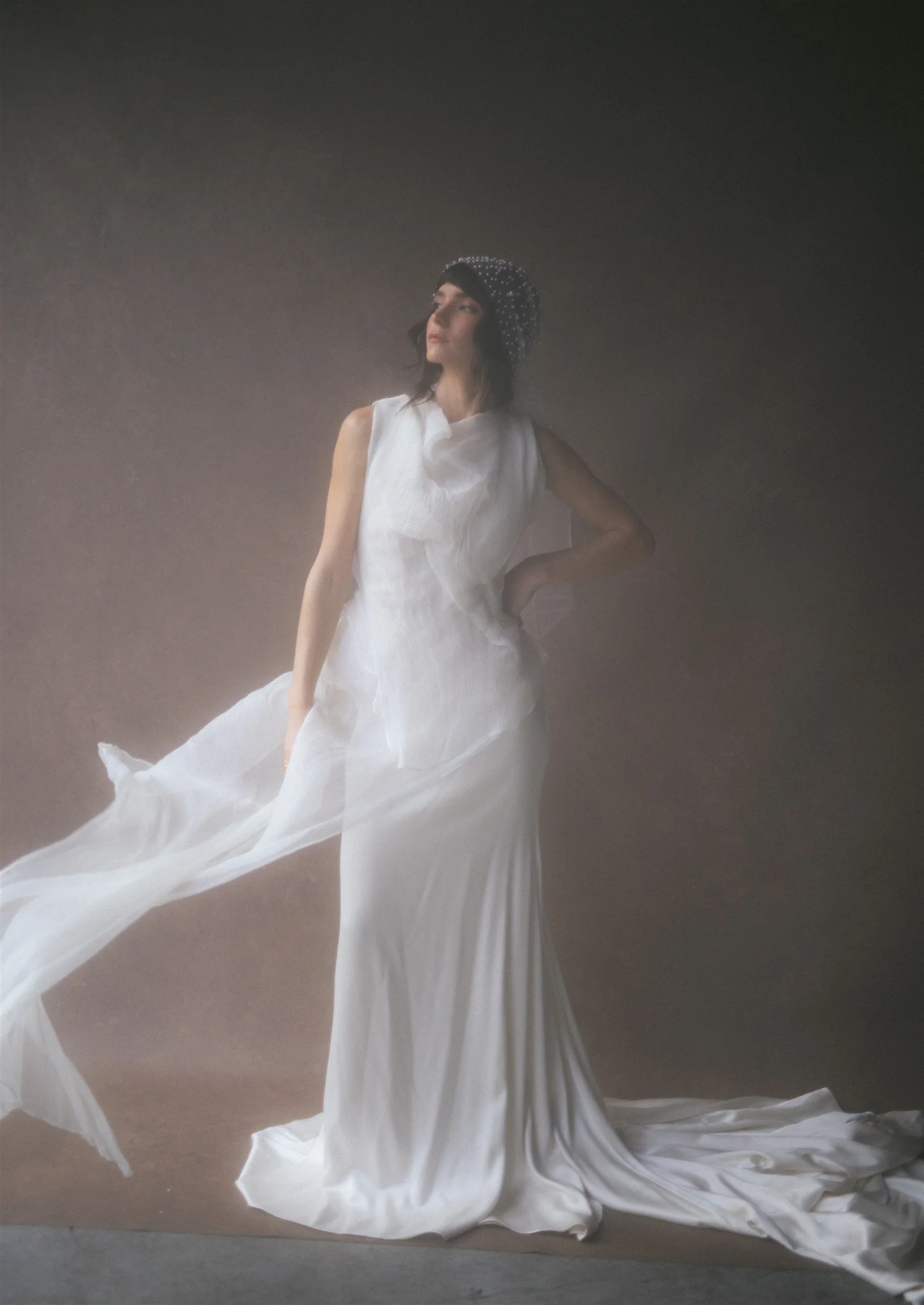 Bride in flowing white silk gown against a warm hand-painted canvas backdrop, train extending across the frame