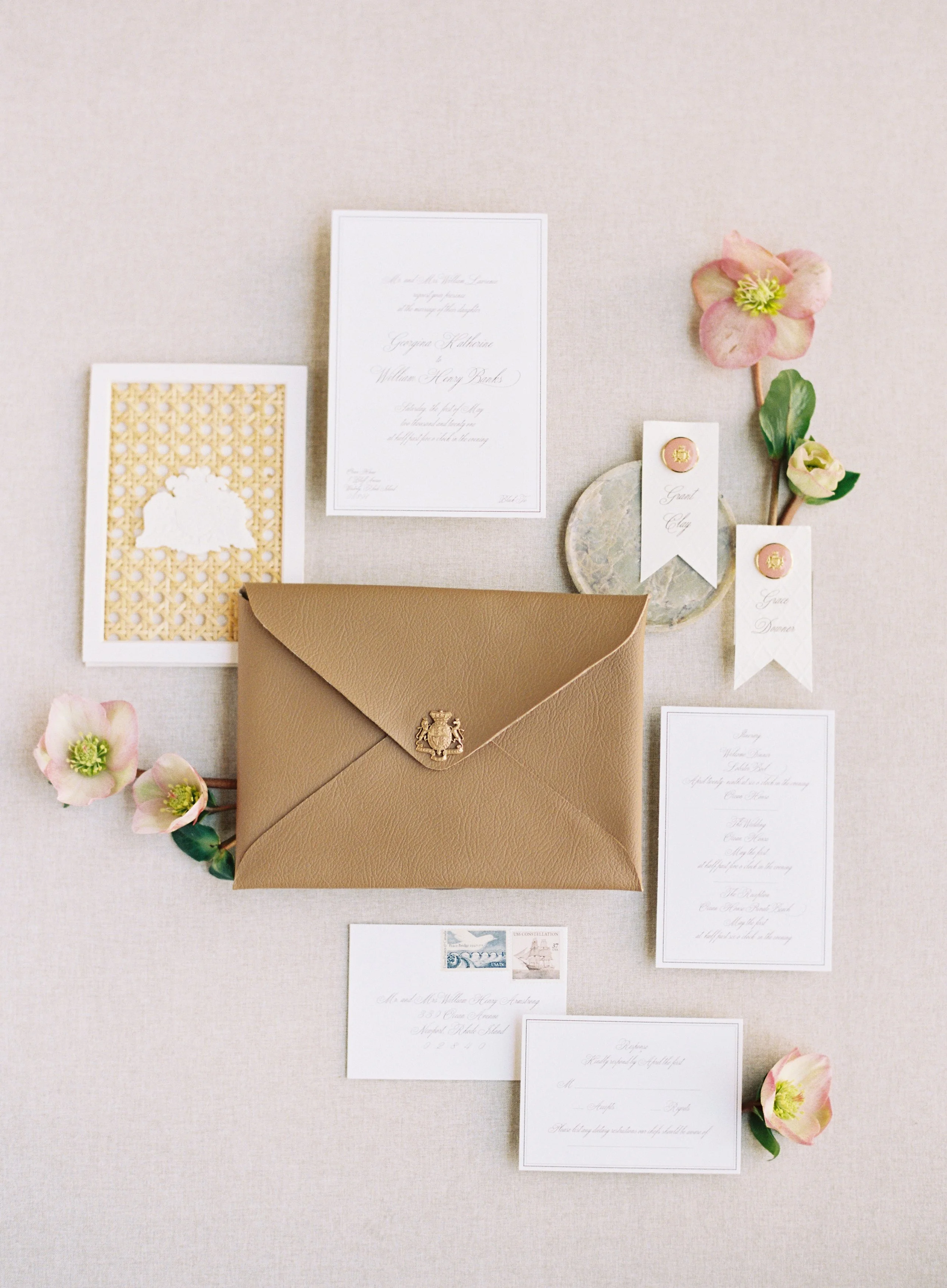 Wedding stationery flat lay featuring leather envelope, wax seals, cane lattice detail, and RSVP card with botanical accents on a warm neutral backdrop