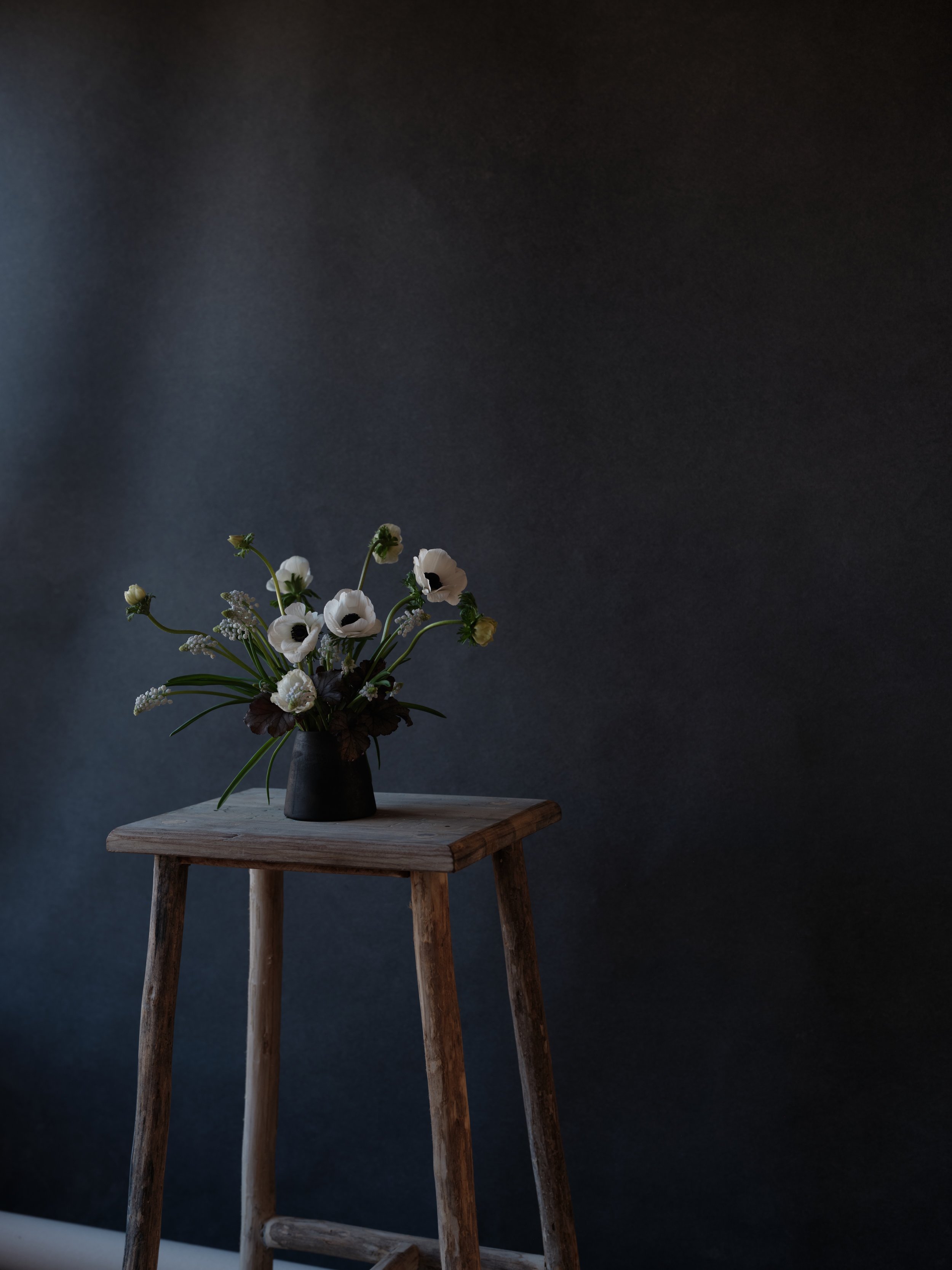 minimalist white floral arrangement on wooden stool against Chasing Stone Carbon backdrop for dramatic product photography