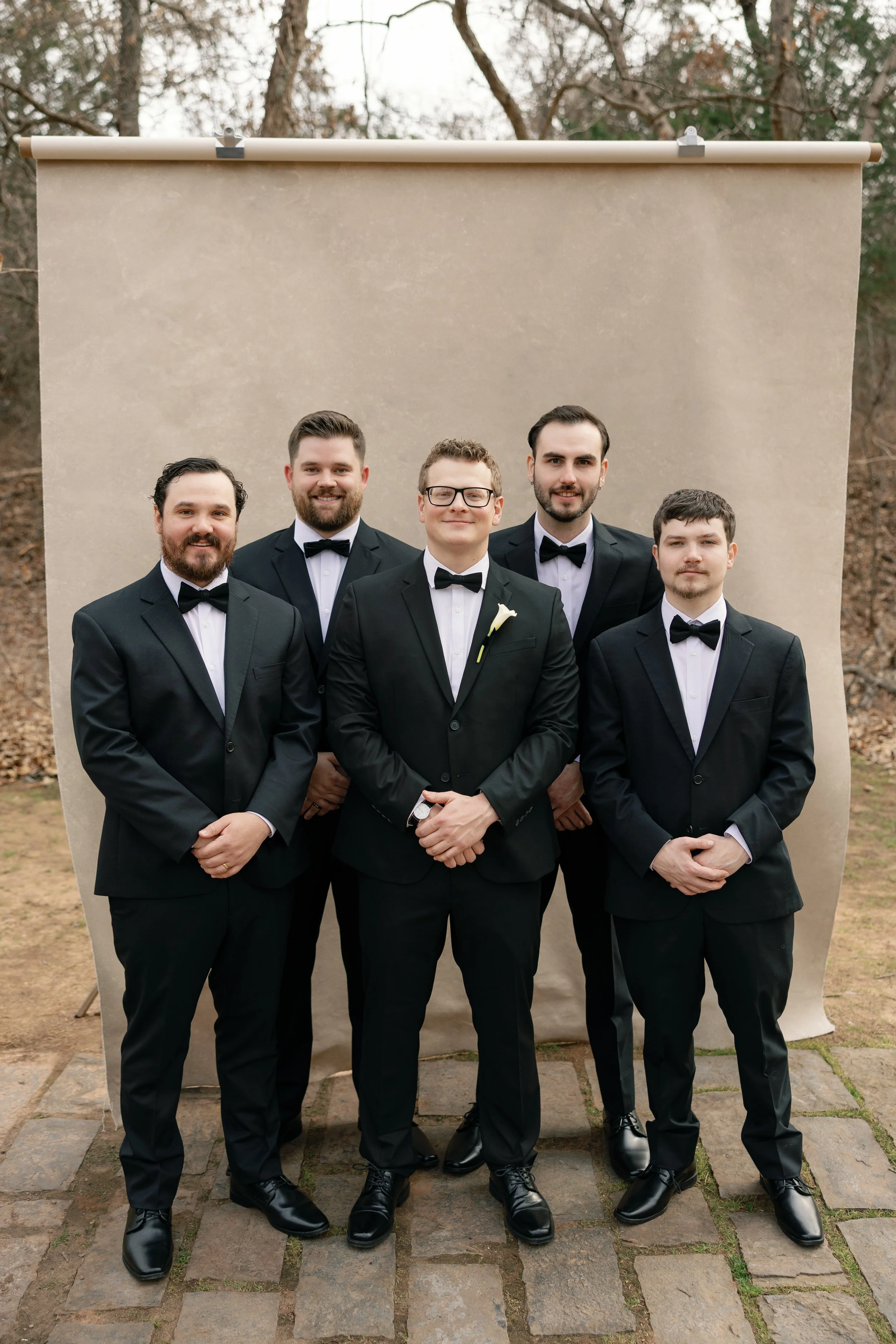 groom and four groomsmen in black tuxedos posing in front of a Chasing Stone Sandstone hand-painted canvas backdrop