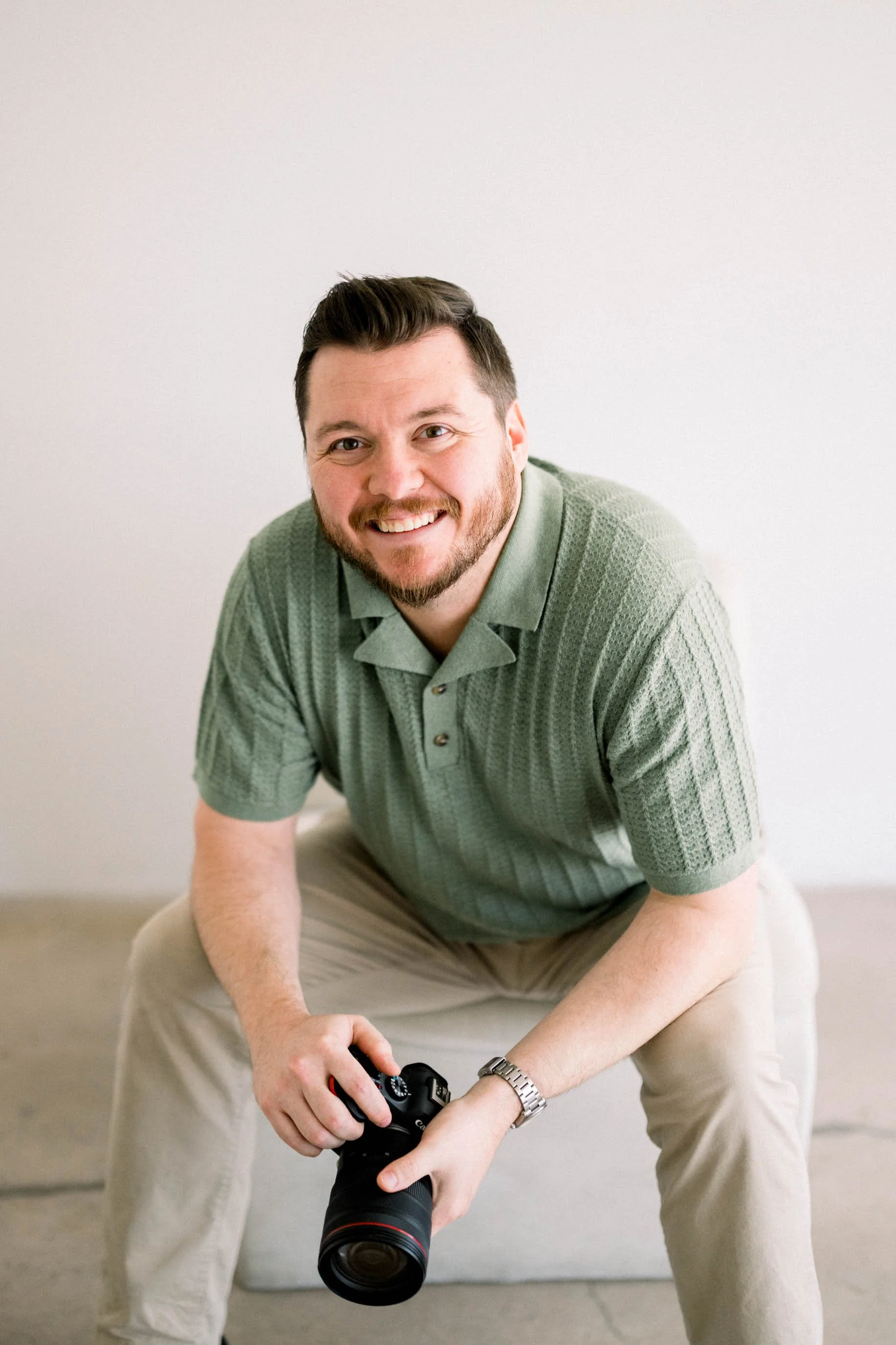 Professional photographer with camera seated against a clean white hand-painted canvas backdrop, illustrating how Chasing Stone backdrops create approachable, polished results for corporate headshot and personal branding photography