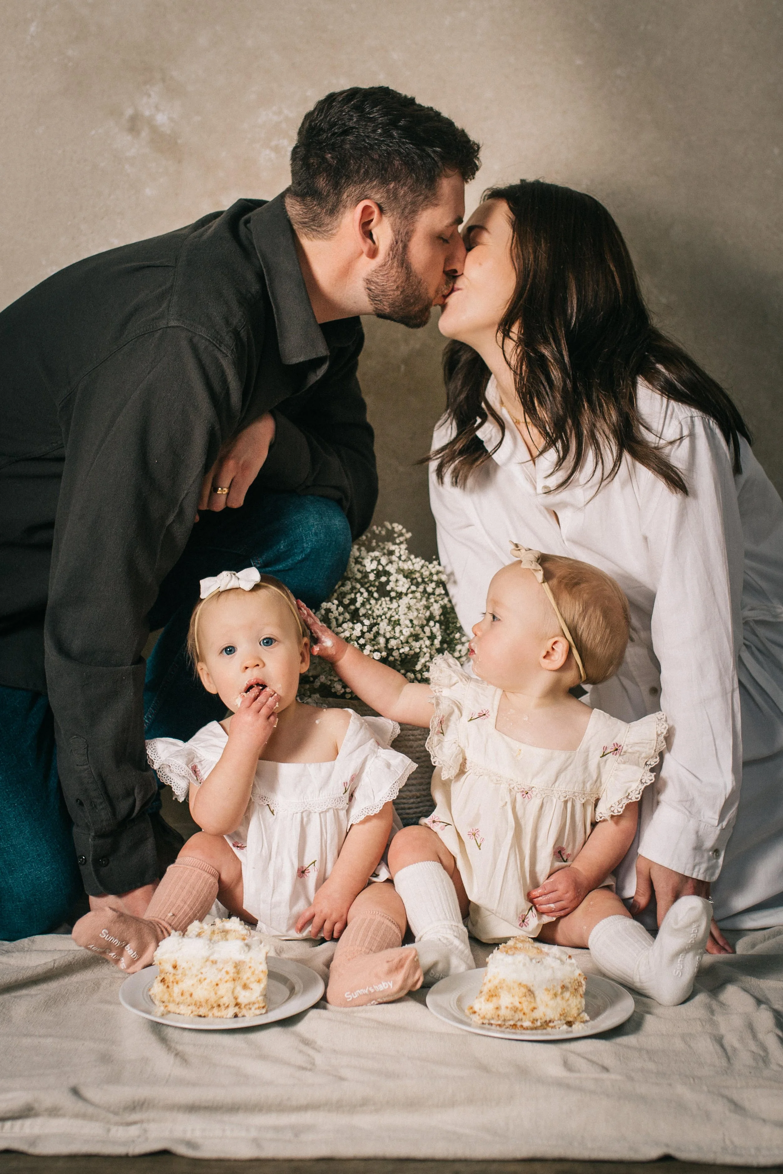 Family mini session portrait with parents and twin babies sitting on a neutral hand-painted backdrop used for seasonal mini session photography