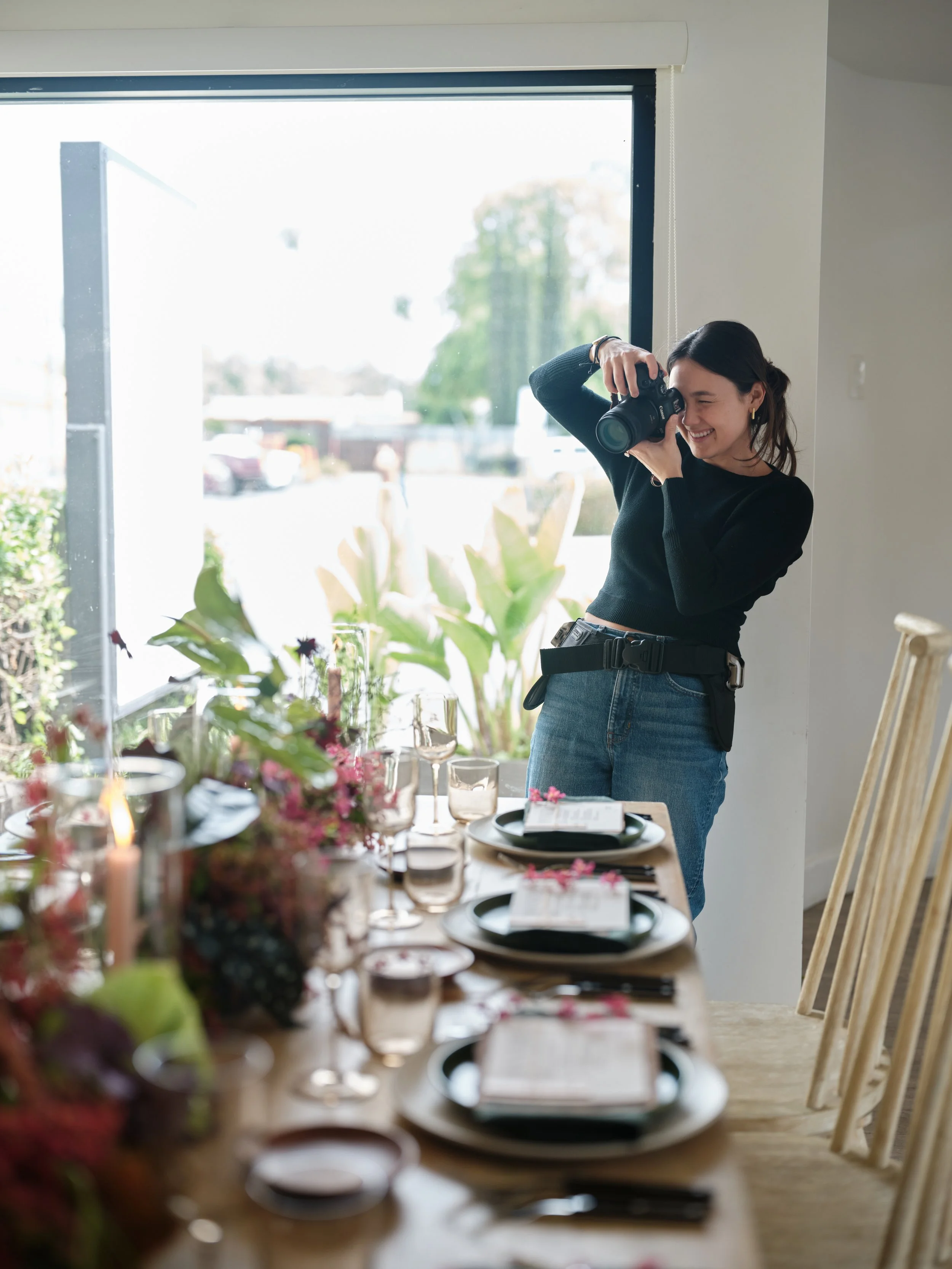 photographer capturing a styled table setting with floral arrangements and glassware near a large window using natural light in a bright studio