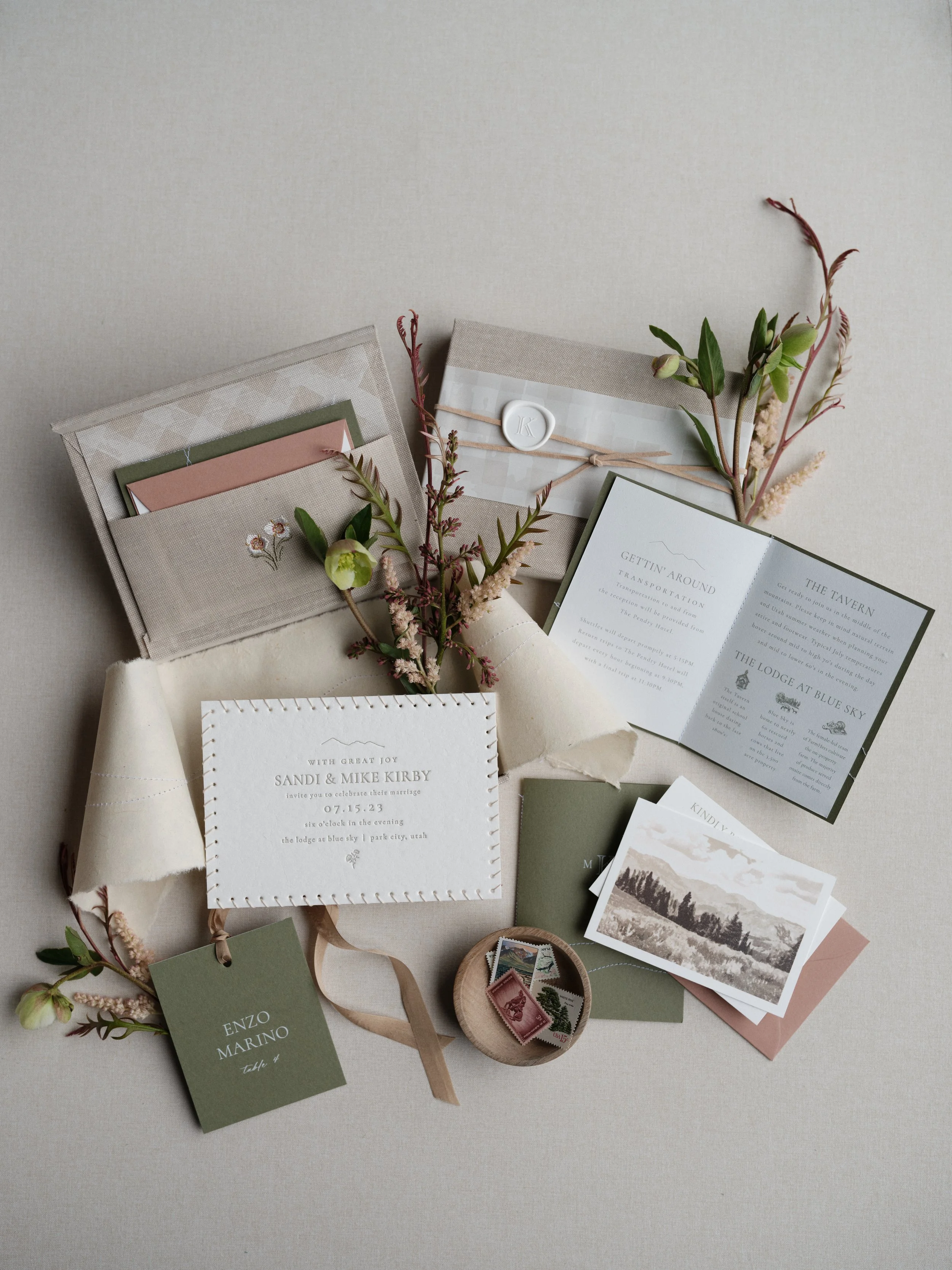 Wedding flat lay photography of a full stationery suite with olive envelopes, wax seal, and botanical details