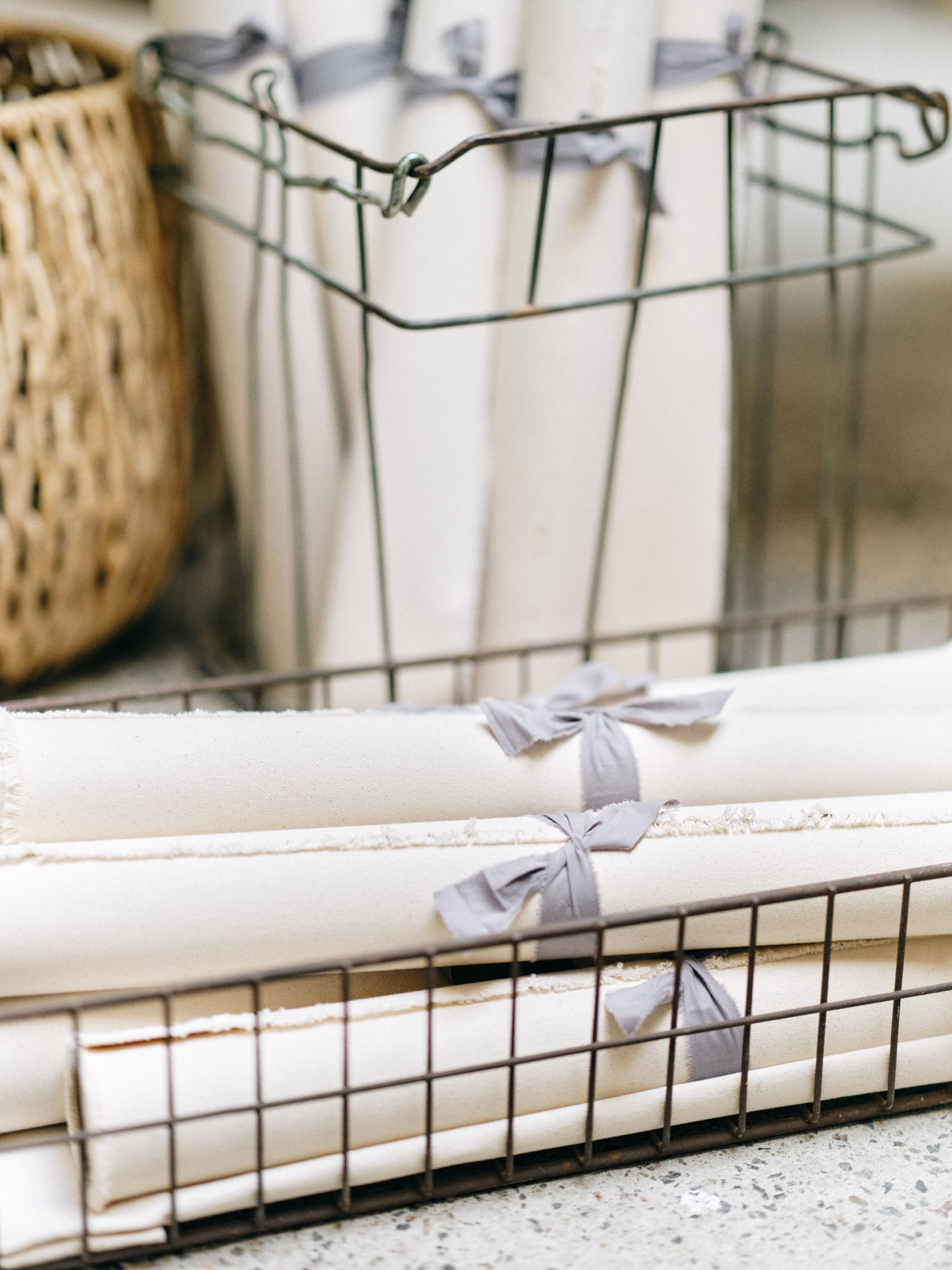 Neutral fabric photography styling surfaces rolled and secured with gray ribbon stored in vintage wire basket