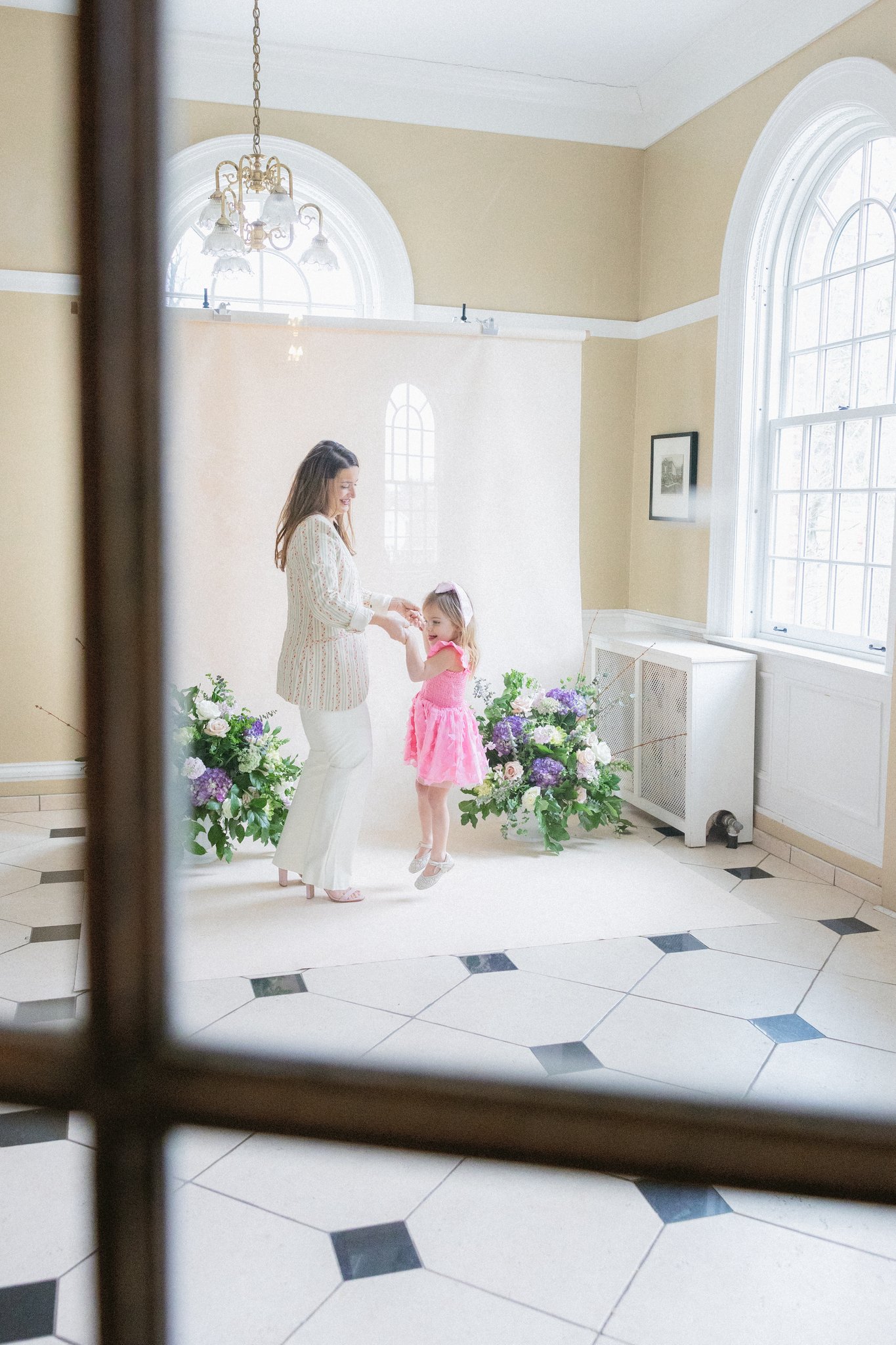 mother and daughter holding hands in front of a white hand-painted canvas backdrop