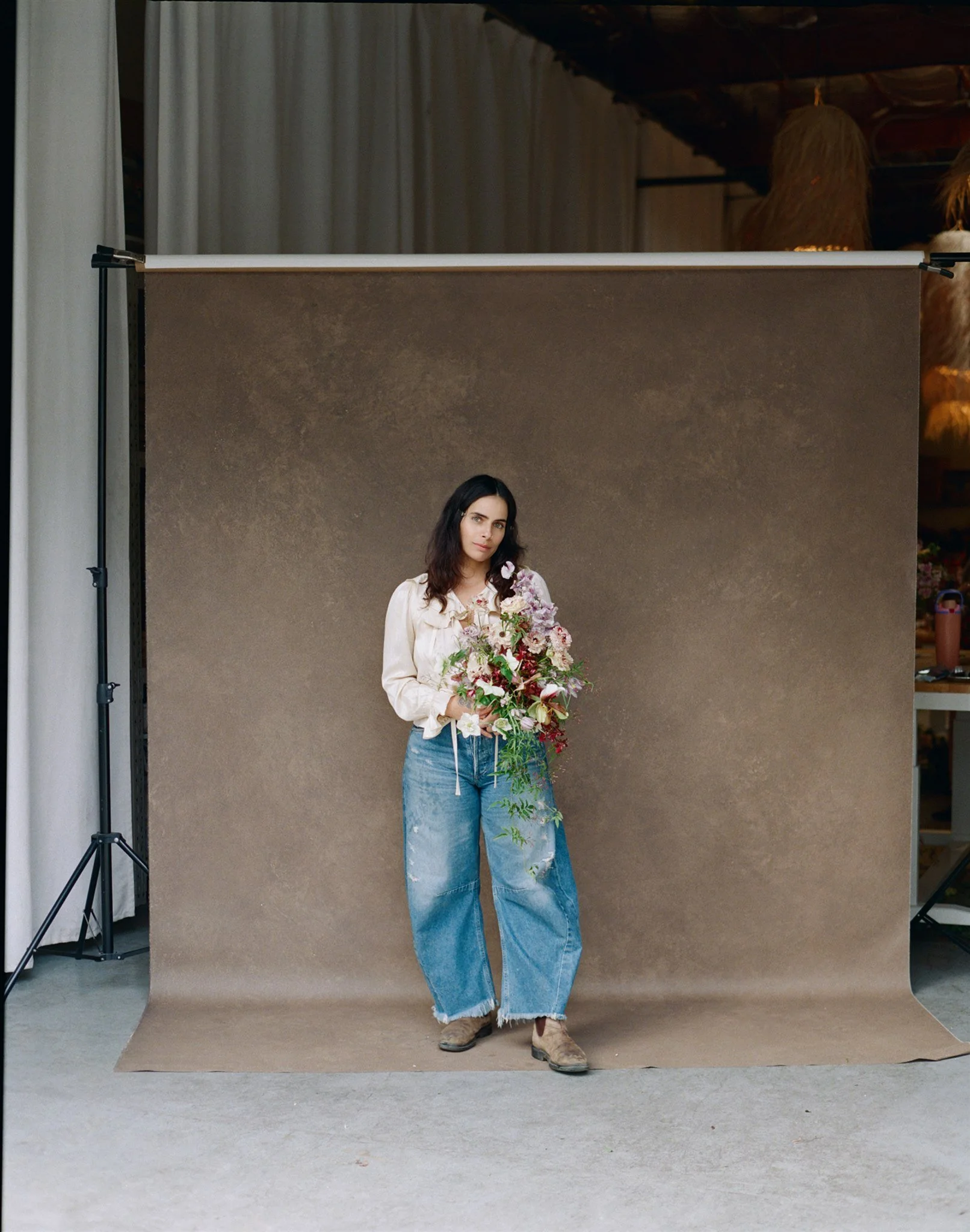 woman holding a floral arrangement while standing in front of a hand-painted brown canvas photography backdrop in a natural light studio setting