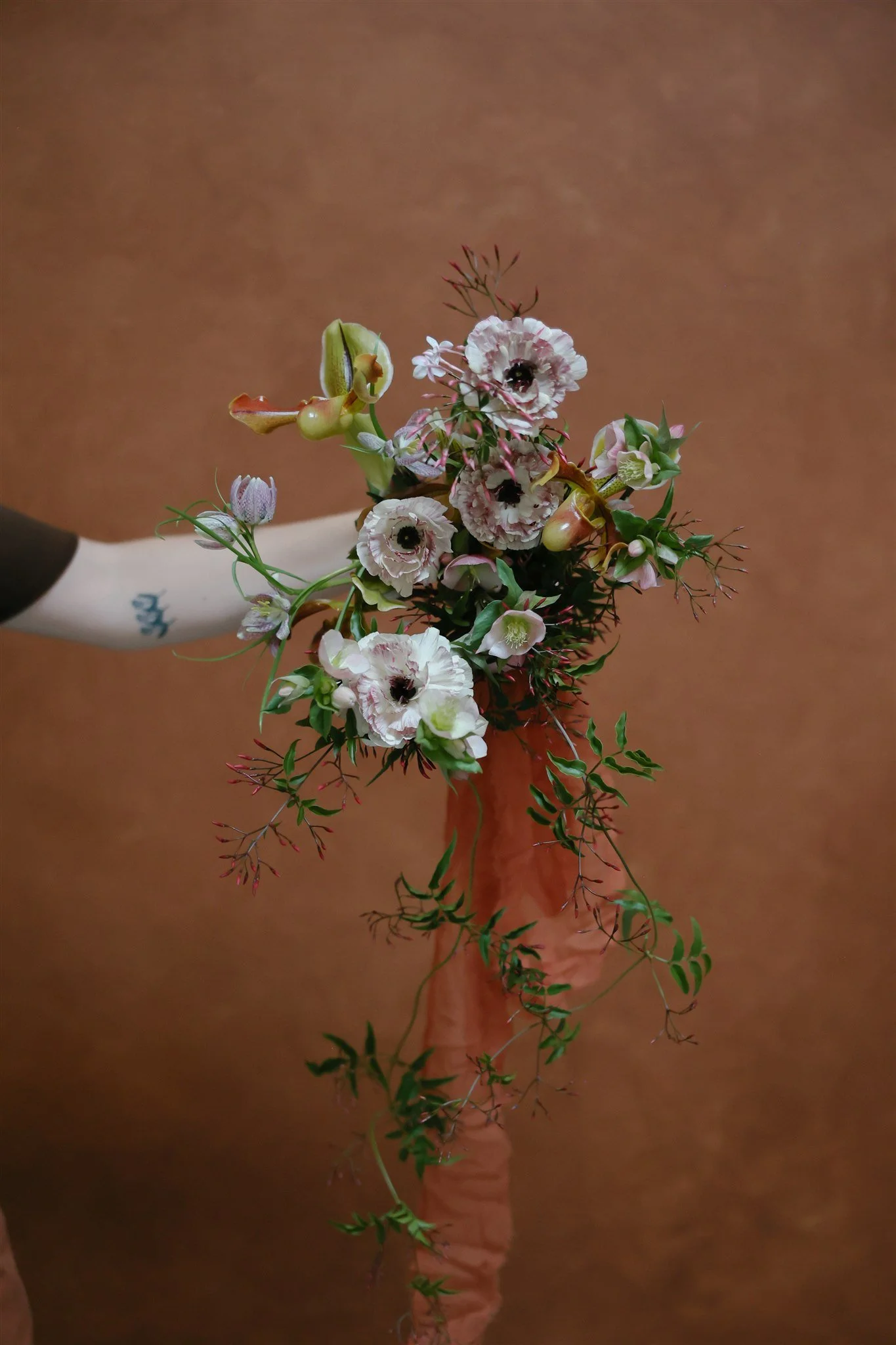 bridal bouquet with ranunculus, anemones, and trailing jasmine against a warm Clay hand-painted canvas backdrop, demonstrating negative space in floral editorial photography