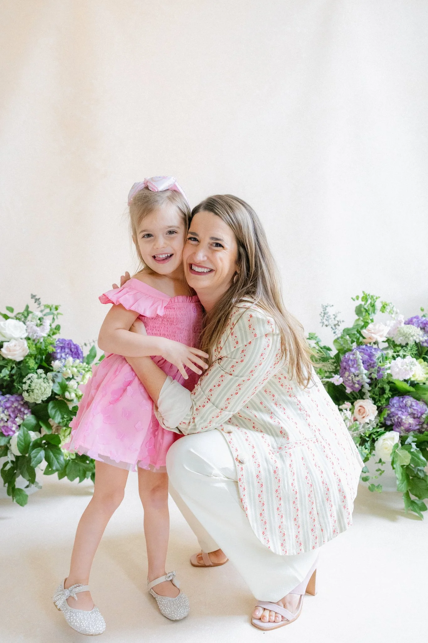 Mother and daughter studio portrait in front of a warm neutral hand-painted canvas backdrop with purple and white floral styling