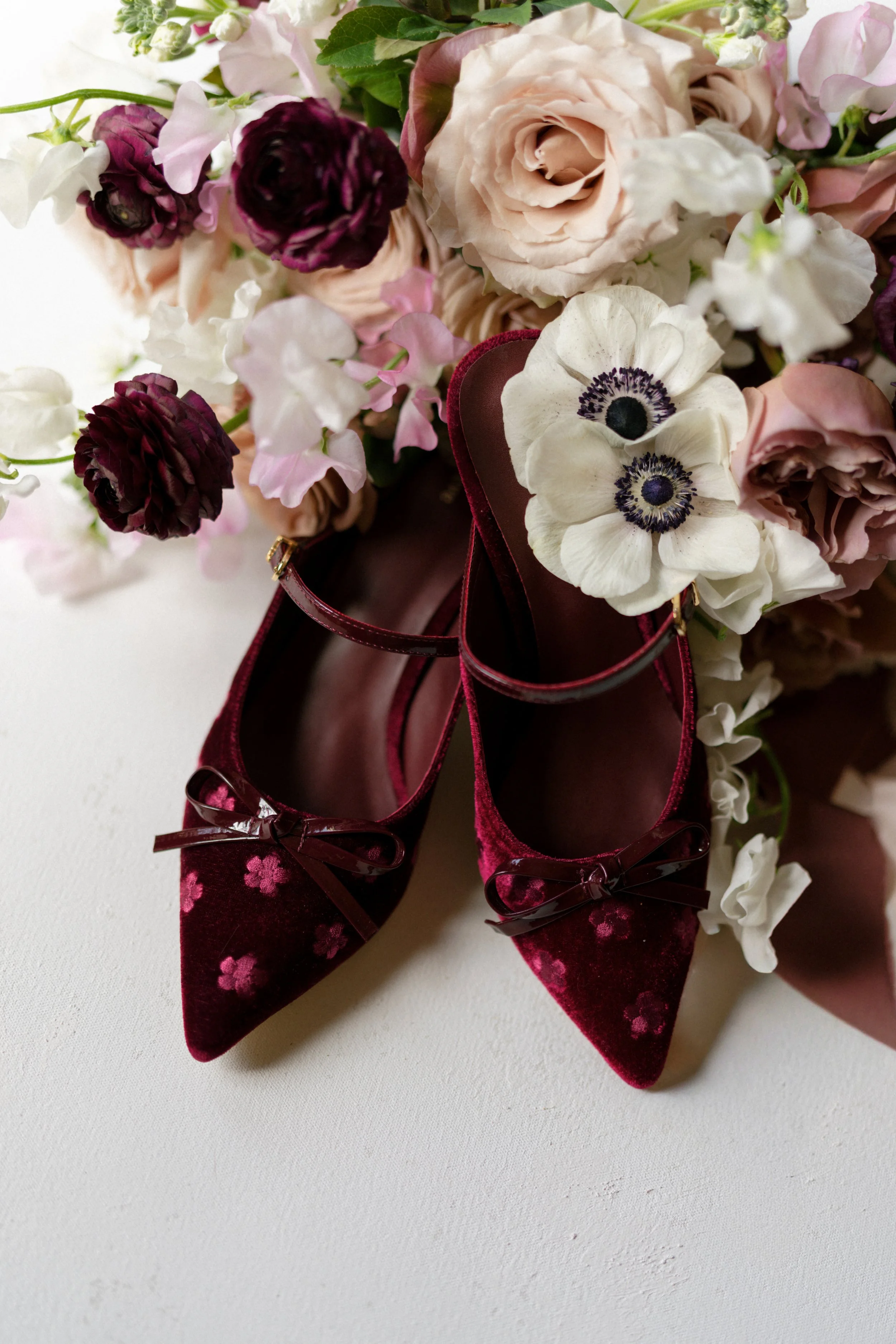 burgundy velvet bridal heels styled with a romantic mauve and cream bouquet on a hand-painted styling surface