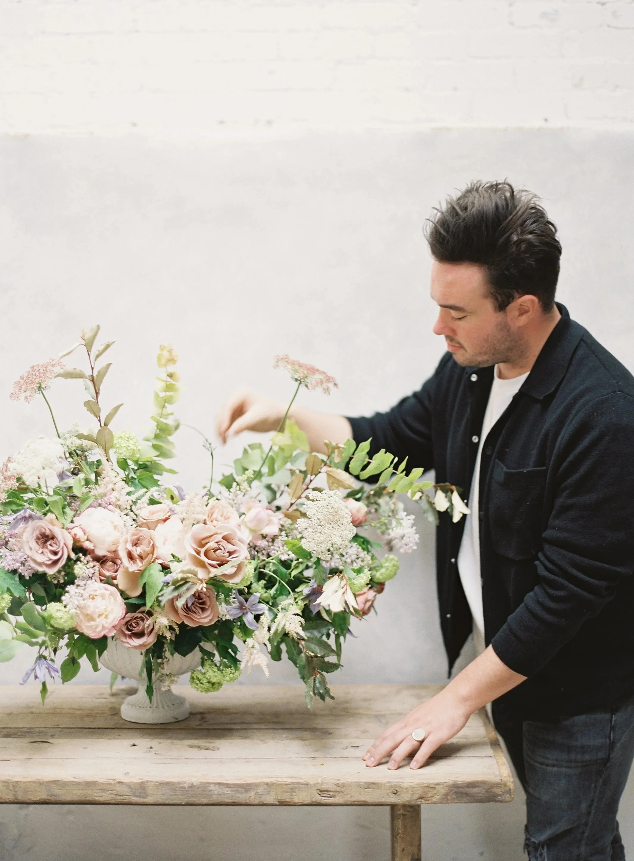 florist arranging a lush blush and mauve floral centerpiece on a rustic wood table in a photography studio