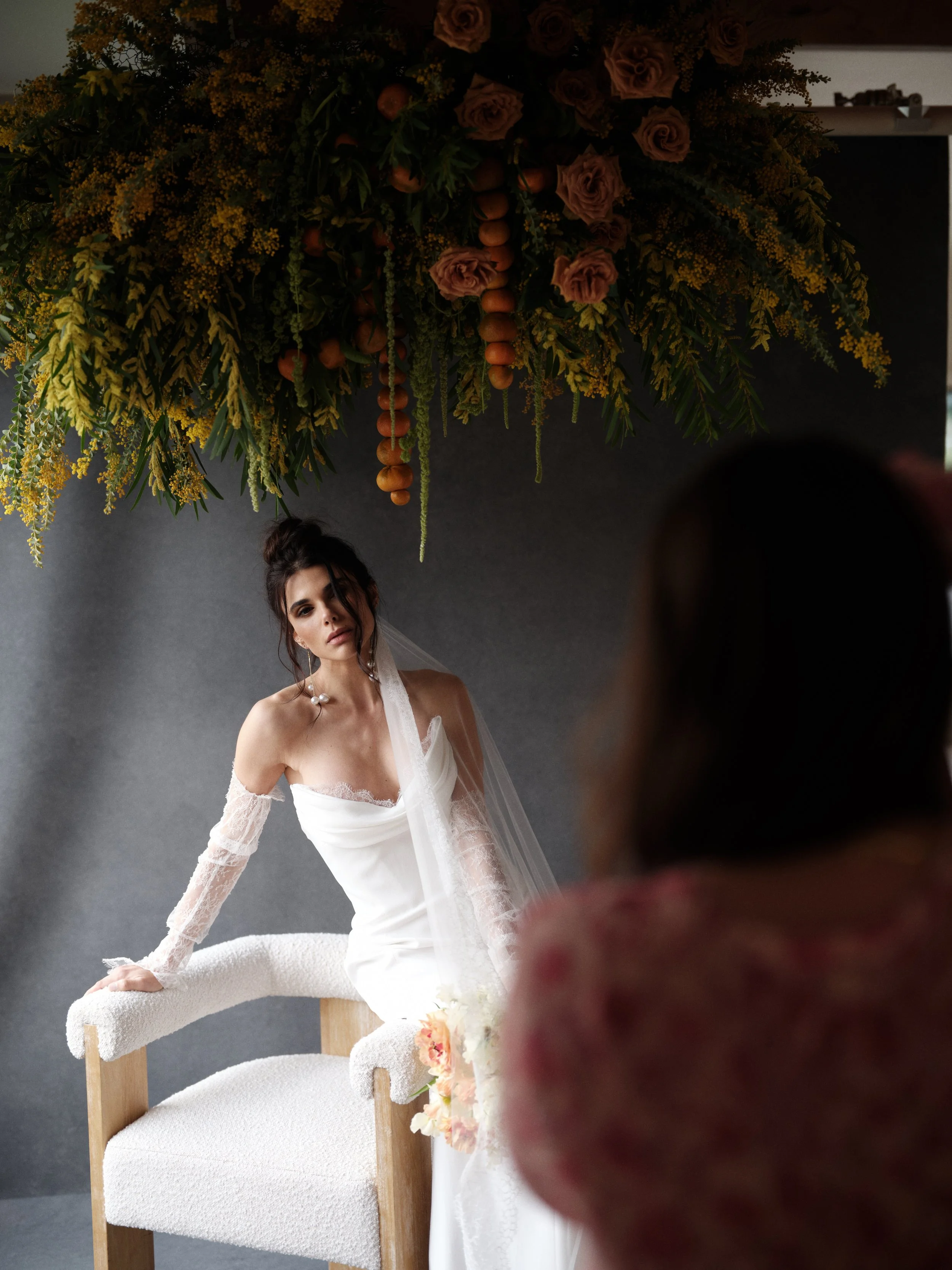 Moody bridal portrait with a dark neutral backdrop and warm overhead floral arrangement showing how intentional color pairing flatters fair skin tones